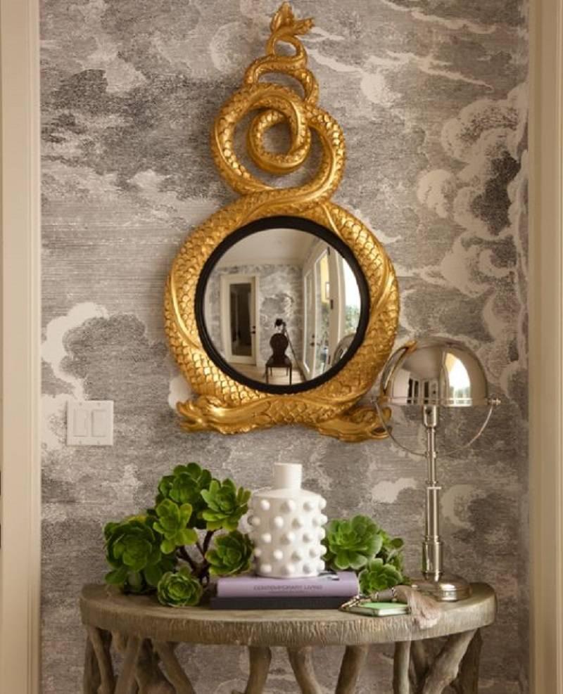 Two mythical dolphins, their tails entwined into a striking crest, encircle a convex mirror. The design is fittingly finished in hand-laid gold leaf over a black bole.