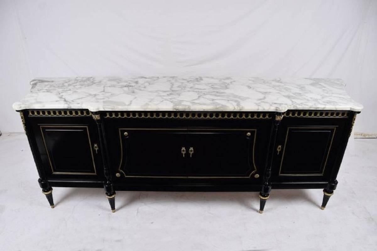 This massive 1950s French Louis XVI style buffet is made of mahogany wood that has been ebonized and a lacquered finish. The facade of the carved facade has brass molding details on the cabinet doors and a band along the top. The four cabinet doors