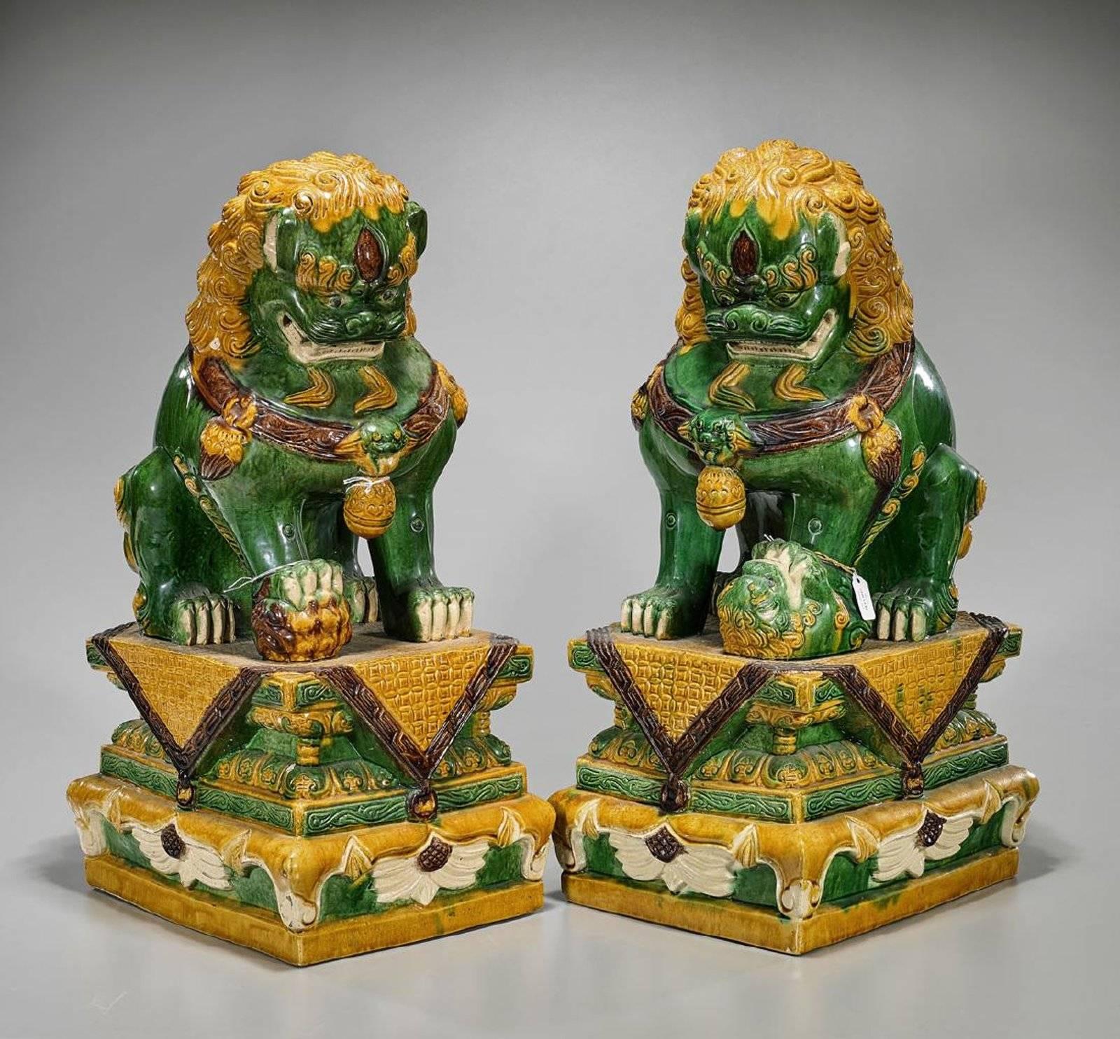 Extremely decorative and colorful pair of Chinese Sancai glazed statues in the form of foo dog lions on resting on pedestals with a ball in their front paws. Each in a mirrored format with open jaws.

Each measures approximately 23