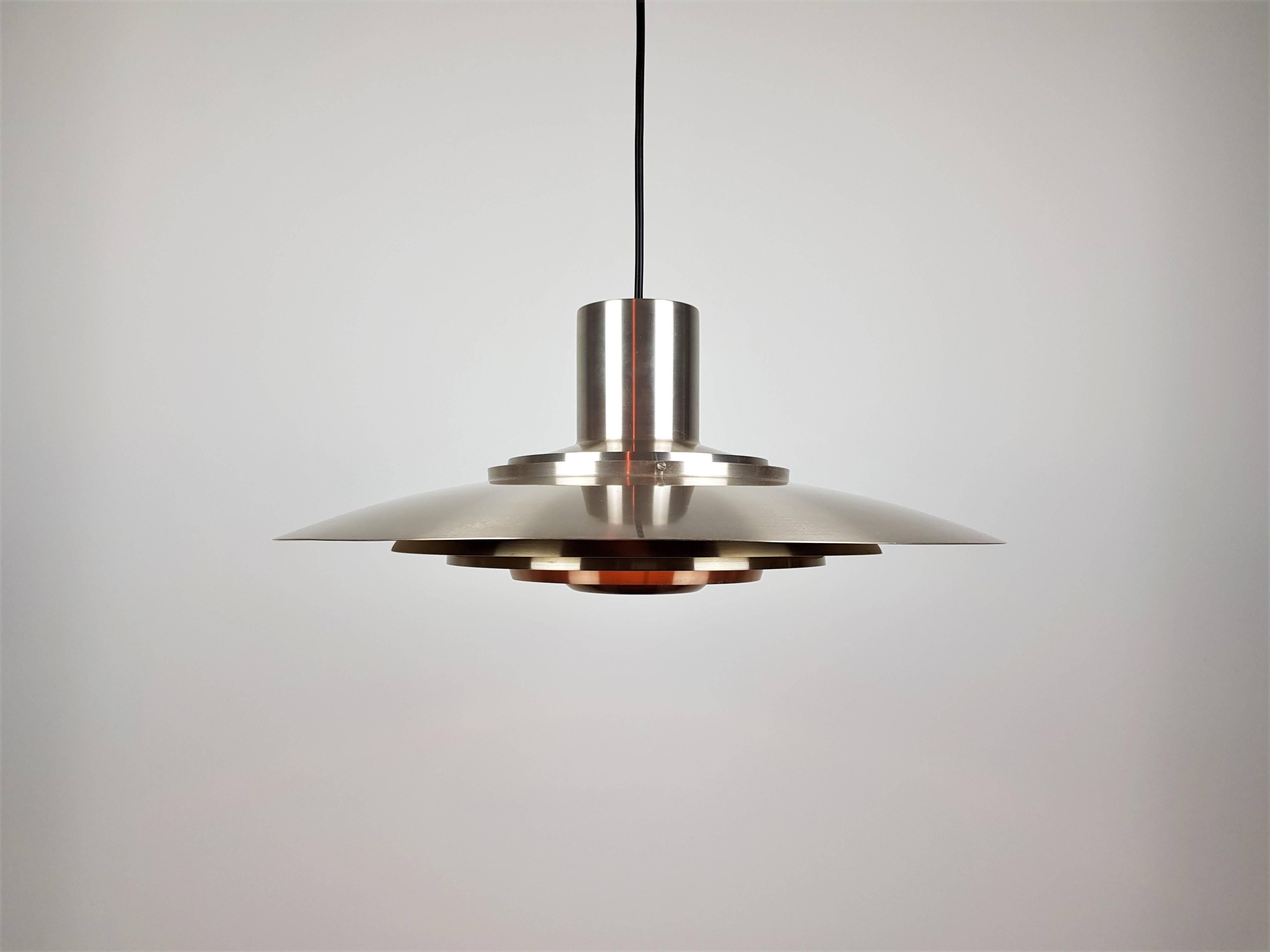A lightly brassed aluminium pendant by Preben Fabricius & Jørgen Kastholm for Nordisk Solar Compagni, 1964.
 
Comprising of five tiers, the decreasing sized tiers obscure any glare and sight of the light bulb resulting in a warm muted light being