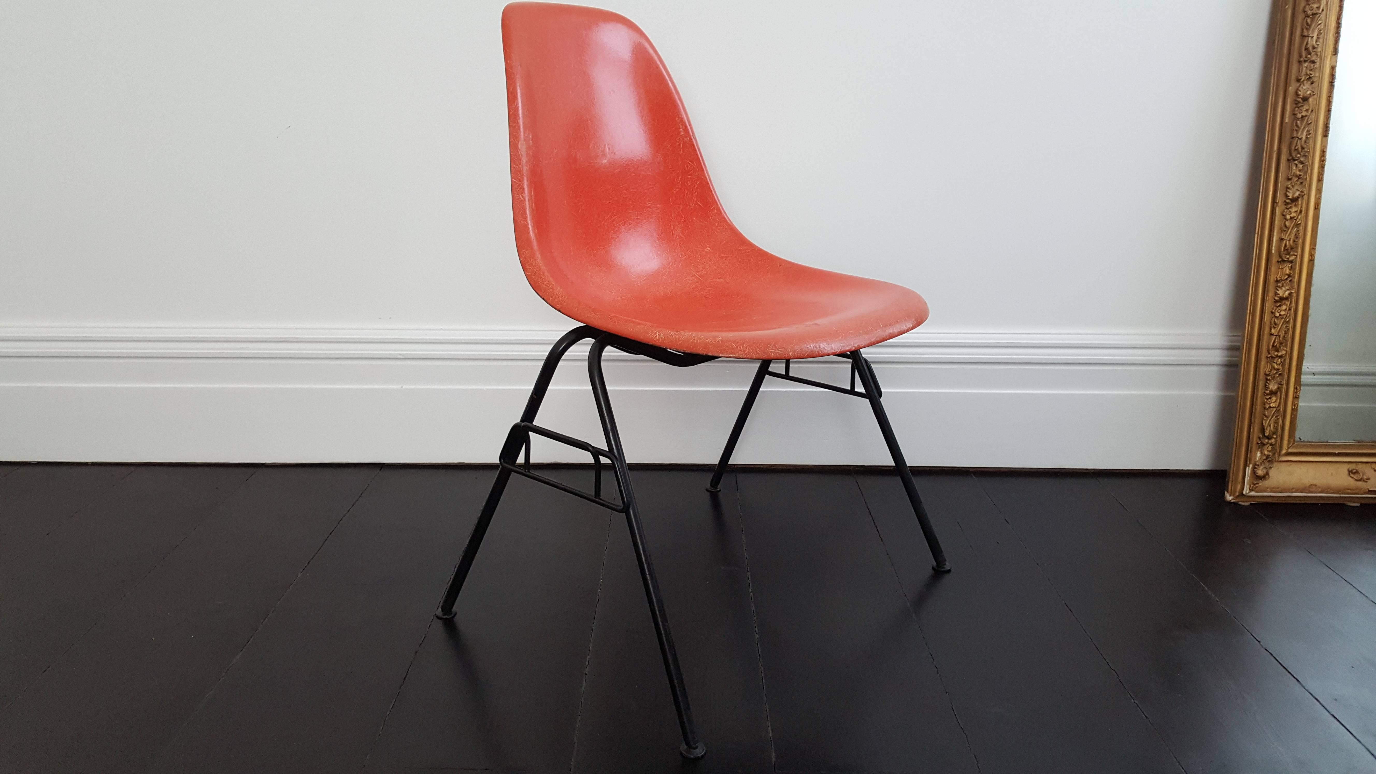 A vibrant deep orange red fibreglass Charles and Ray Eames designed Herman Miller DSS stacking chair with black base.