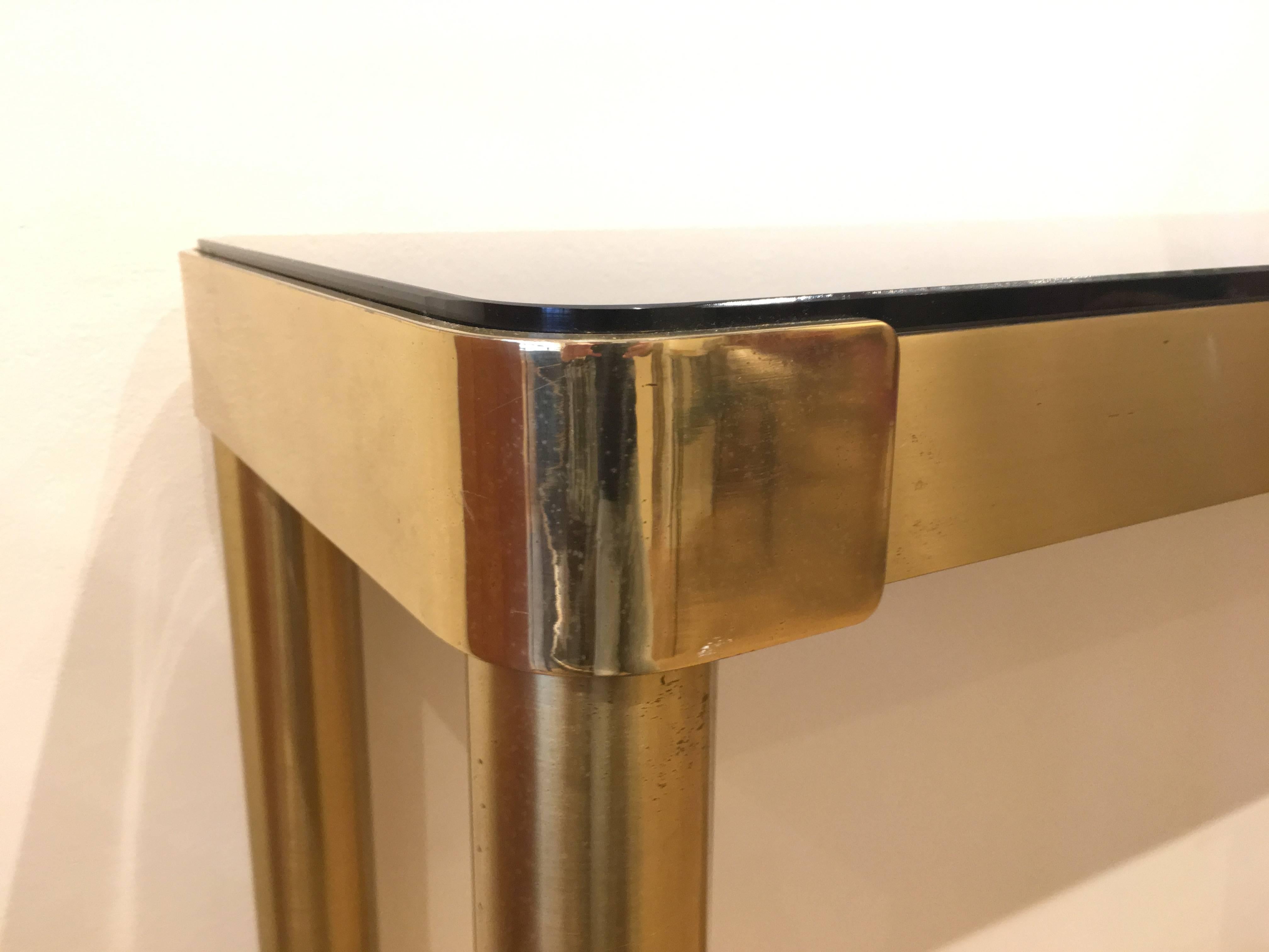 An elegant Italian console in brass, with smoke brown mirror top. It dates circa 1970s. Simple lines for great refinement.