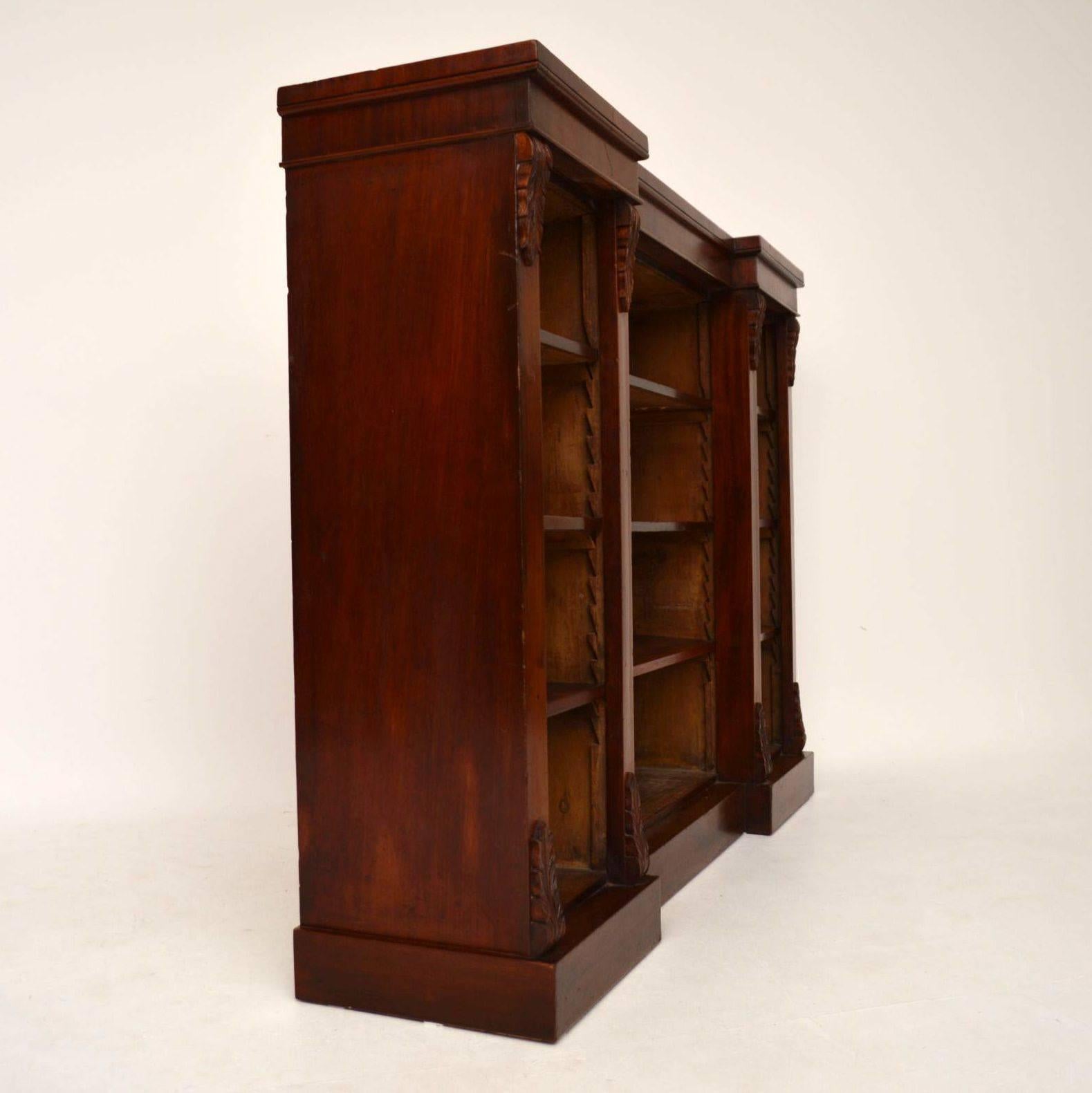 Antique Victorian mahogany dwarf bookcase with an inverted breakfront and carved corbels top and bottom. It's in good condition and has adjustable shelves on sharks teeth supports. This bookcase sits on a plinth base & has the original pine panelled