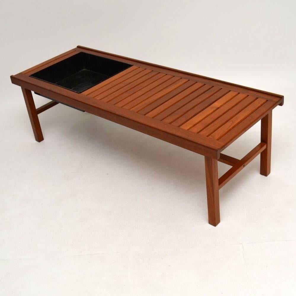 A very stylish and unusual Danish teak coffee table / bench, this dates from around the 1960s. It has a metal tray on one side that lifts in and out, originally designed as a plant holder but can equally be used as a recessed drinks compartment to