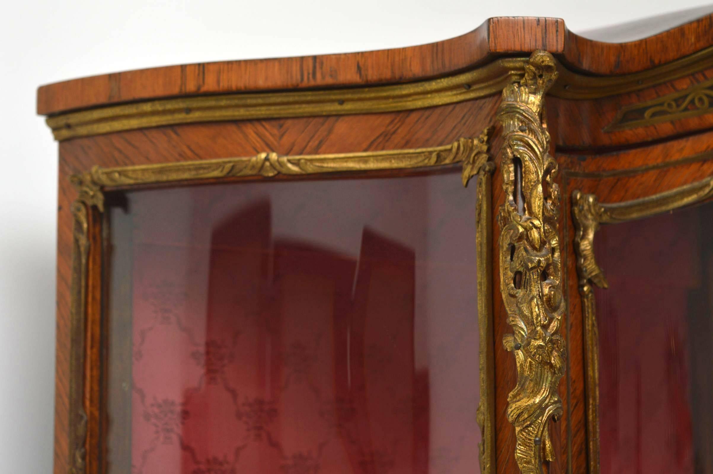 Antique French display cabinet in either Kingwood or Rosewood, with brass inlays & faux boulle bottom panels. It's has a serpentine shaped front and the shaped glass on the front door and sides are original. This display cabinet is in lovely