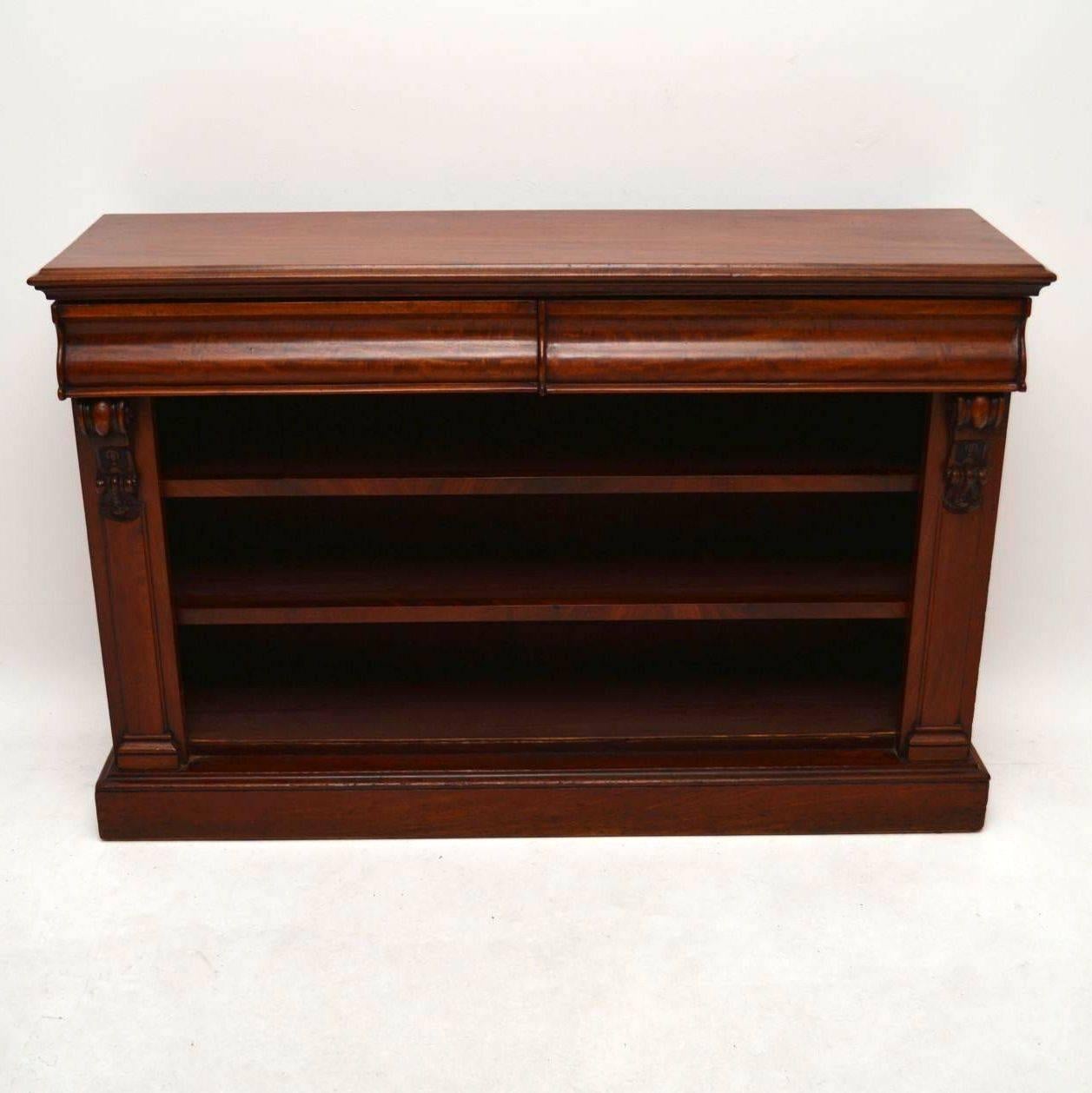 Antique early Victorian mahogany low open bookcase with two shaped drawers on the top. There are two shelves and bold side panels with carved corbels. This piece is in good condition and dates from circa 1840s-1860s period. It's a strong looking