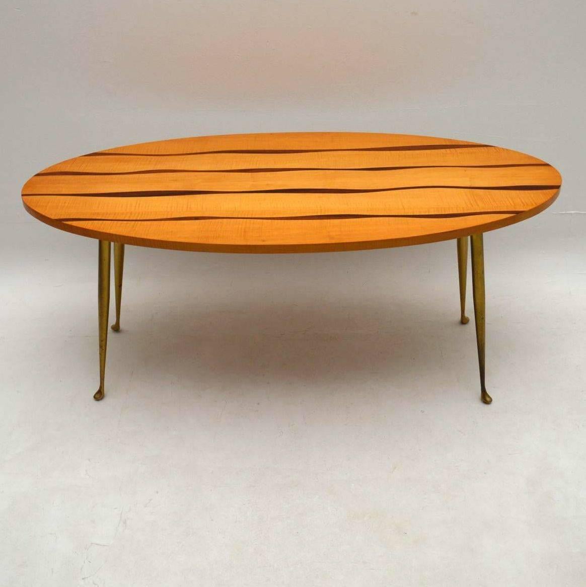 A beautiful and very unusual coffee table from the 1950s, this was imported from Italy. It has a gorgeous design, with an oval top that's made from Satin Wood, and very interesting exotic wood inlay. The table sits on lovely brass legs. We have had