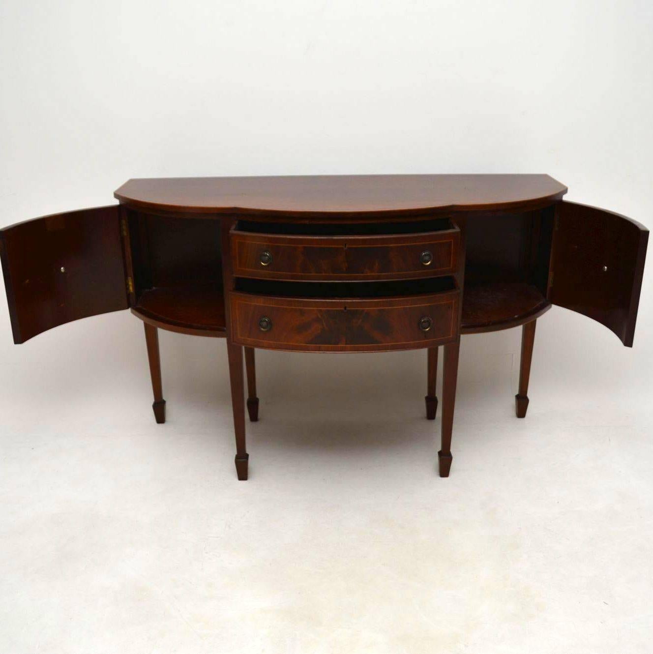 Very elegant fine quality antique mahogany sideboard dating from around the 1910s-1920s period and in lovely condition. It has a kind of serpentine shape and many fine features. The top is cross banded and beautifully inlaid around the edge with