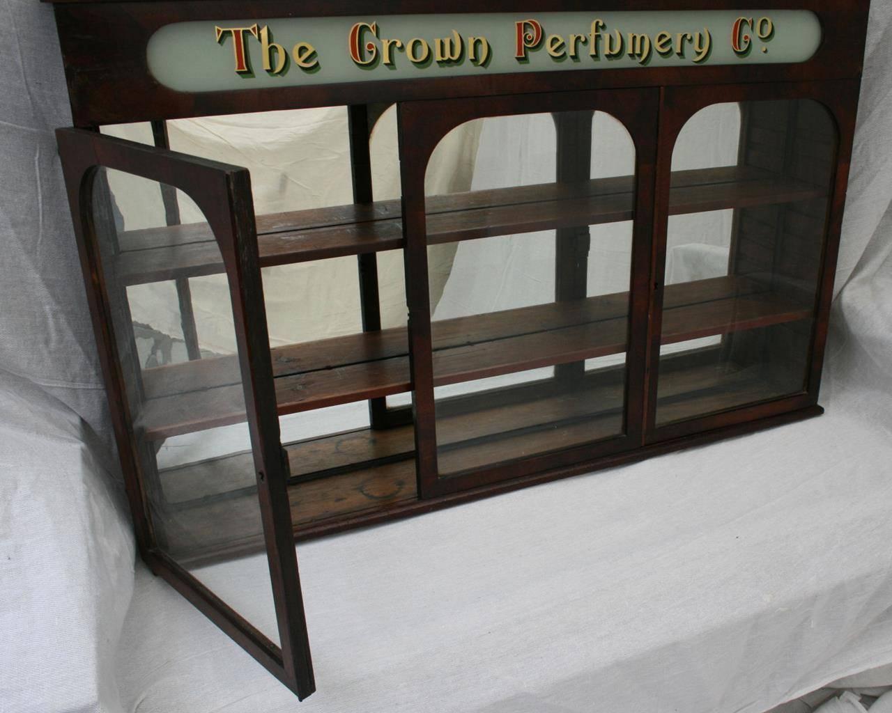 Victorian antique 19th century three-door pharmacy cabinet with a sliding door to the centre and two hinged doors left and right. Original antique wavy glass doors and original glass advertising pediment advertising The Crown Perfumery Co. This