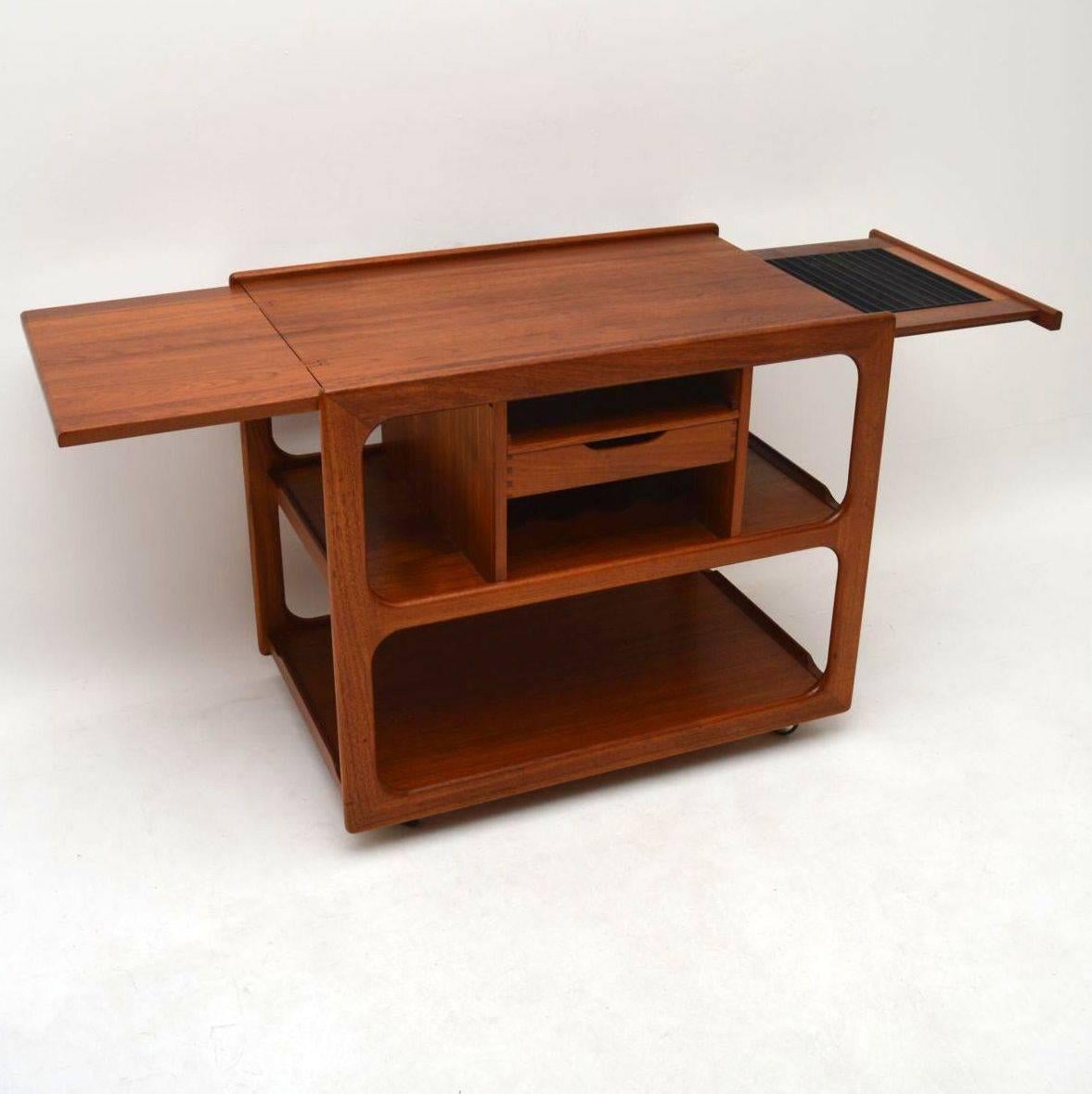 A top quality and very stylish vintage teak drinks trolley, this was made in Denmark and dates from the 1960s-1970s. It has a drop down extending leaf on one side, and a pull-out slide with an inbuilt metal grill on the other. This rolls smoothly on