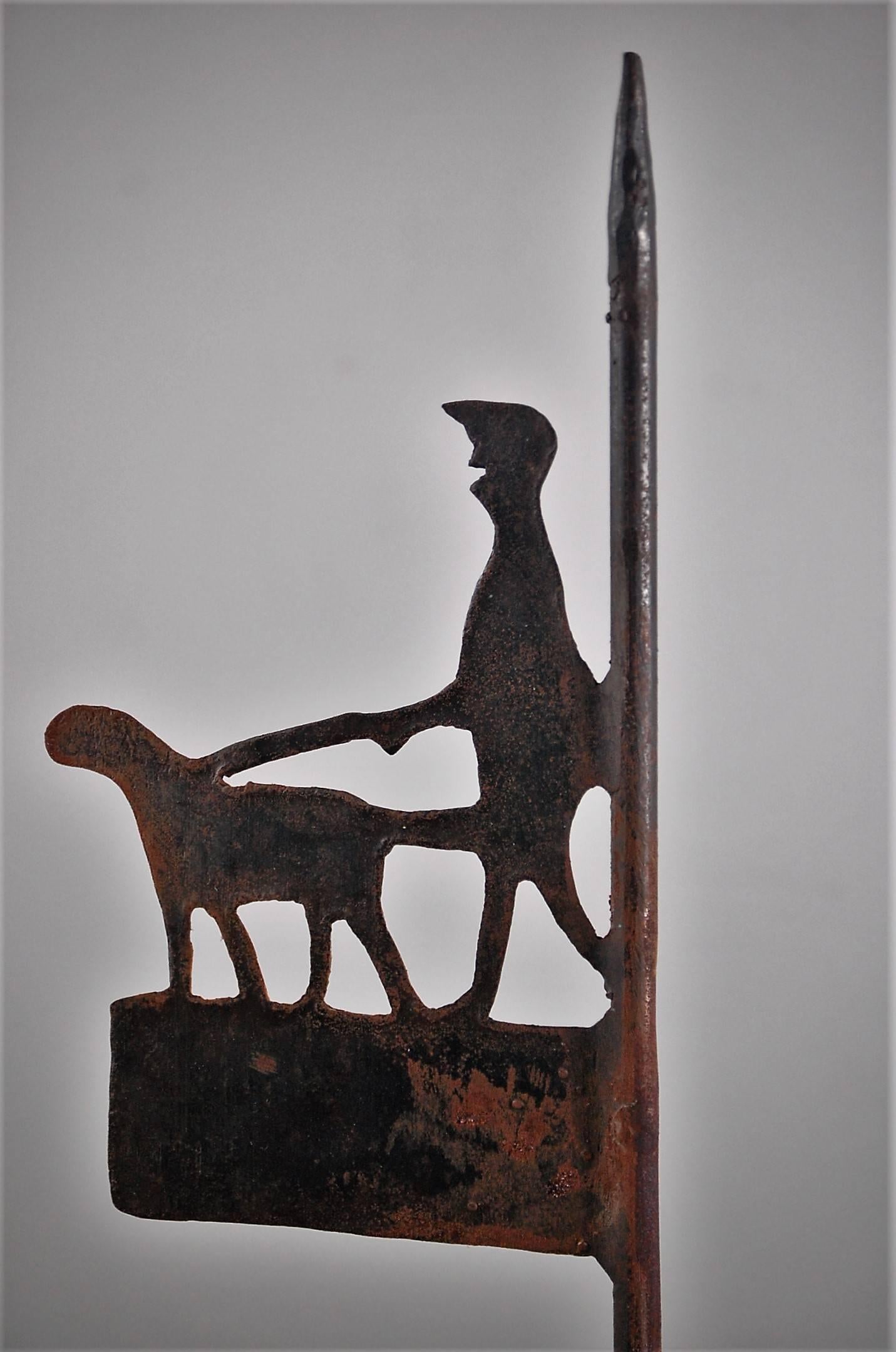 20th century diminutive weathervane or finial from a dog kennel, suitably small proportions, naively made, painted sheet metal, depicting a gentleman walking his dog on a leash. Some paint loss in places, sourced in France. Later simple wood stand.