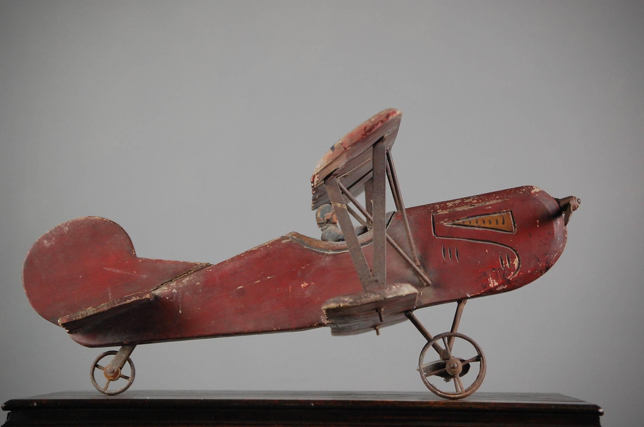 Large 20th century toy biplane, wonderfully playworn with distressed paint finish, all original. predominantly wood construction with metal supports, propeller, pilot and wheels. Mounted on a later steel Stand to give the impression of flight.