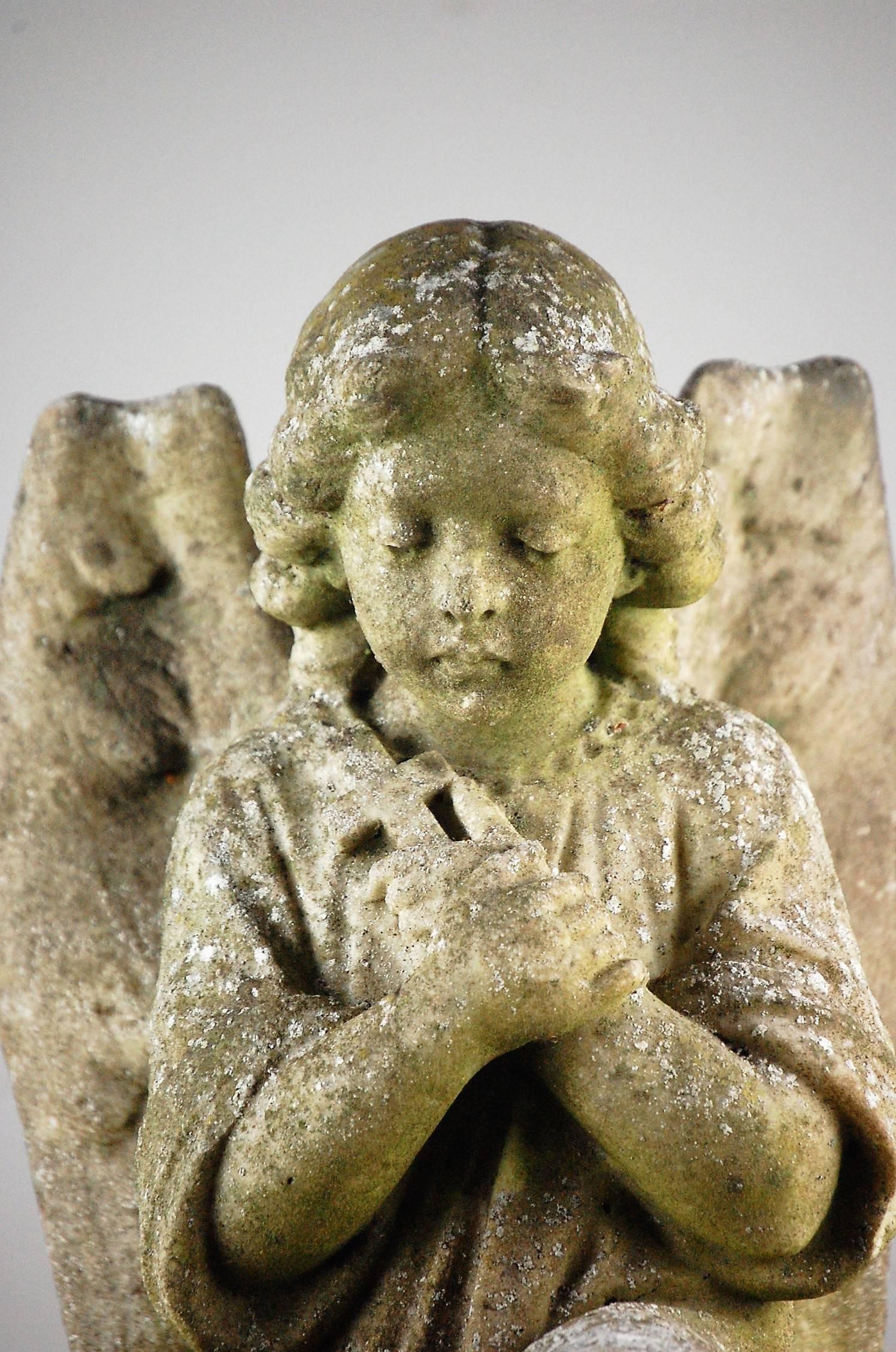 Weathered marble angel kneeling on a tasselled cushion in prayer clutching a cross. Wonderful detail in carving. Late 19th century, French.