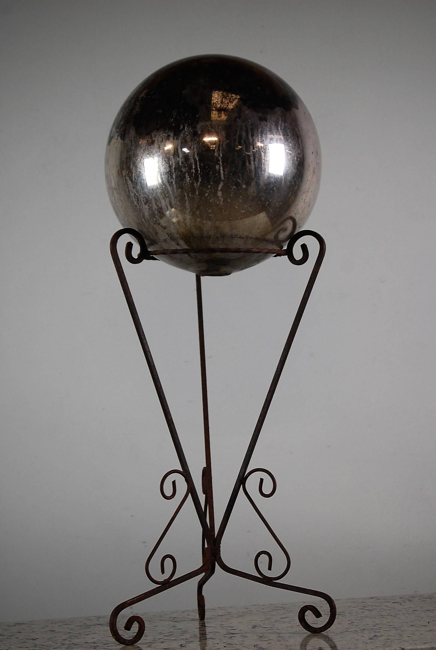 Large, heavily distressed handblown 19th century glass witches ball, the mirror is heavily distressed with approximately 50% Mirror covering remaining. Wonderful mysterious macabre look and feel. Later wrought iron stand.