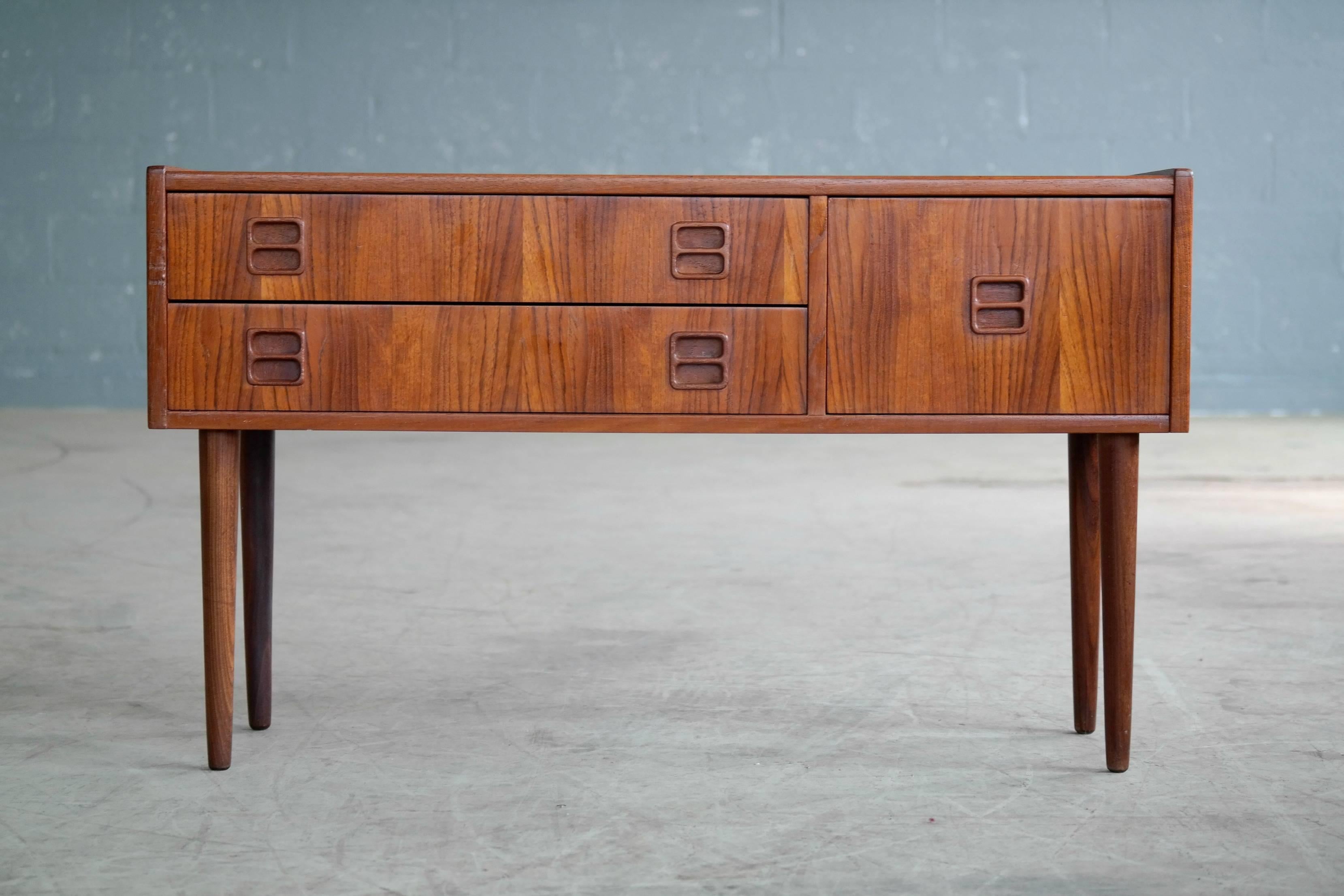 Unusual low console or chest of drawers in teak by Kai Kristiansen. Beautiful color and grain with carved pulls. Unique drawer configuration. Low and wide cabinet on tall legs in solid teak creating a very elegant look. Very versatile with multiple