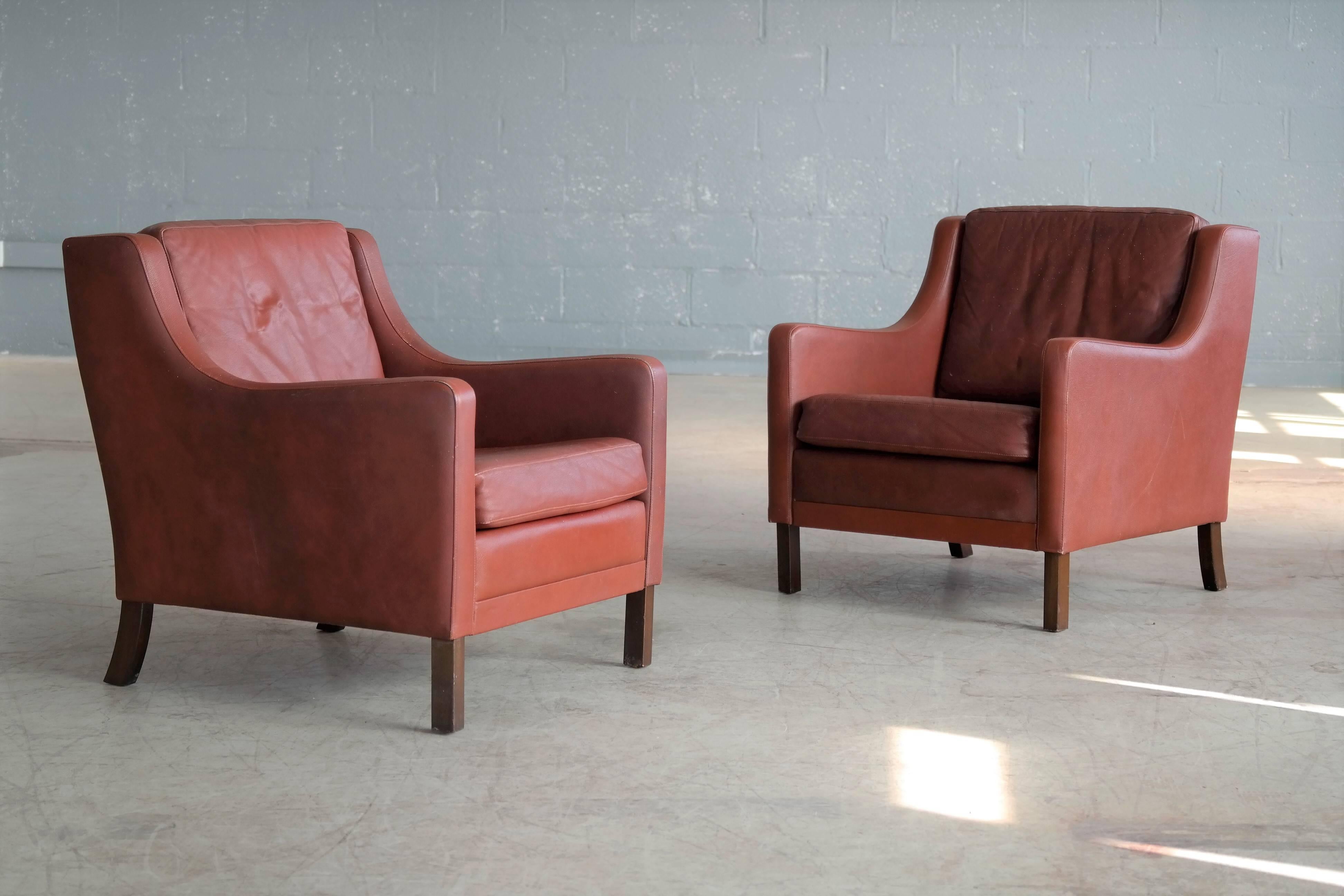 Classic Danish lounge chairs similar to Børge Mogensen’s model 2207 made by Georg Thams in reddish brown leather and stained beech wood legs. Age appropriate patina and wear. Good condition, great deal.