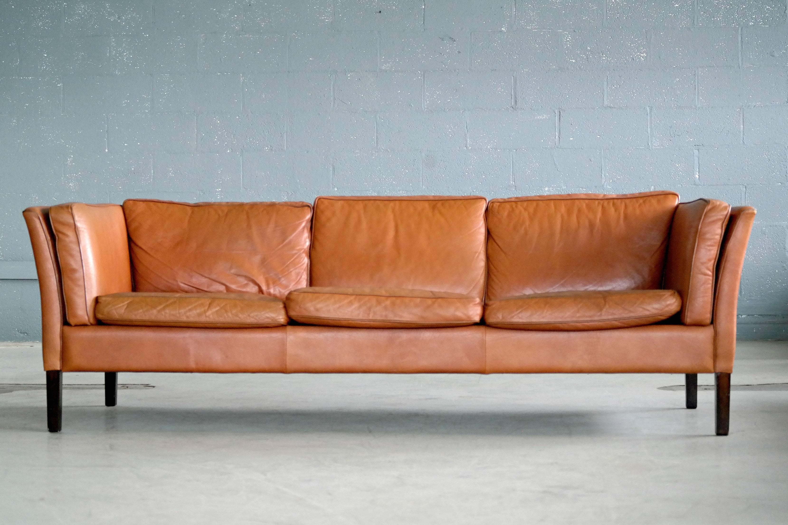 Stunning classic Børge Mogensen style three-seat sofa in supple soft patinated cognac colored leather raised on stained beech wood legs made by Stouby Mobler. Late 1960s design but probably manufactured in the 1970s. Very high build quality that