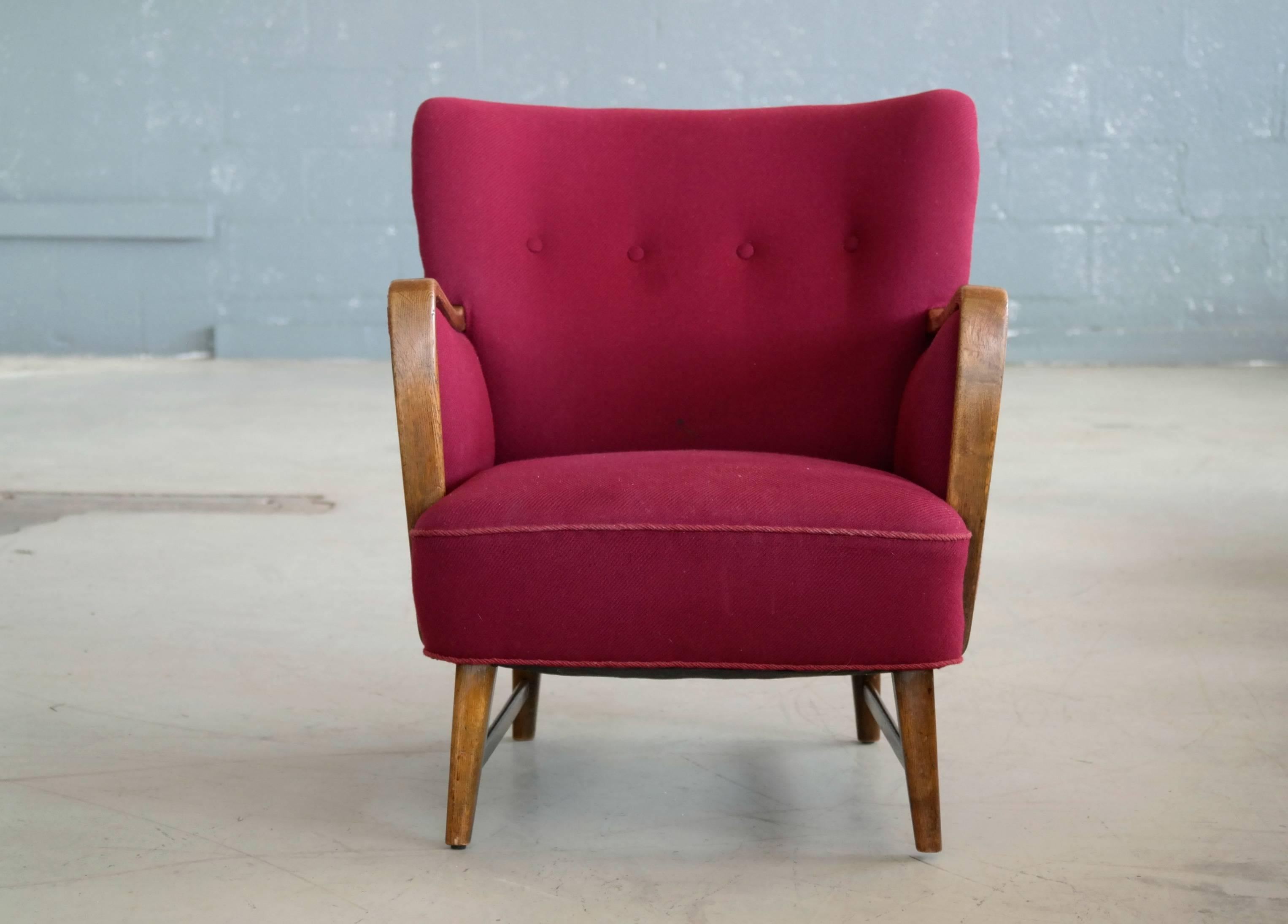 Super charming 1950s lounge chair in a magenta colored wool with armrests and base in a nice golden solid oak. Designed by Kurt Olsen around 1950 for N.A. Jorgensen. N.A. Jorgensen became known as Bramin Mobler in 1958 well known for making