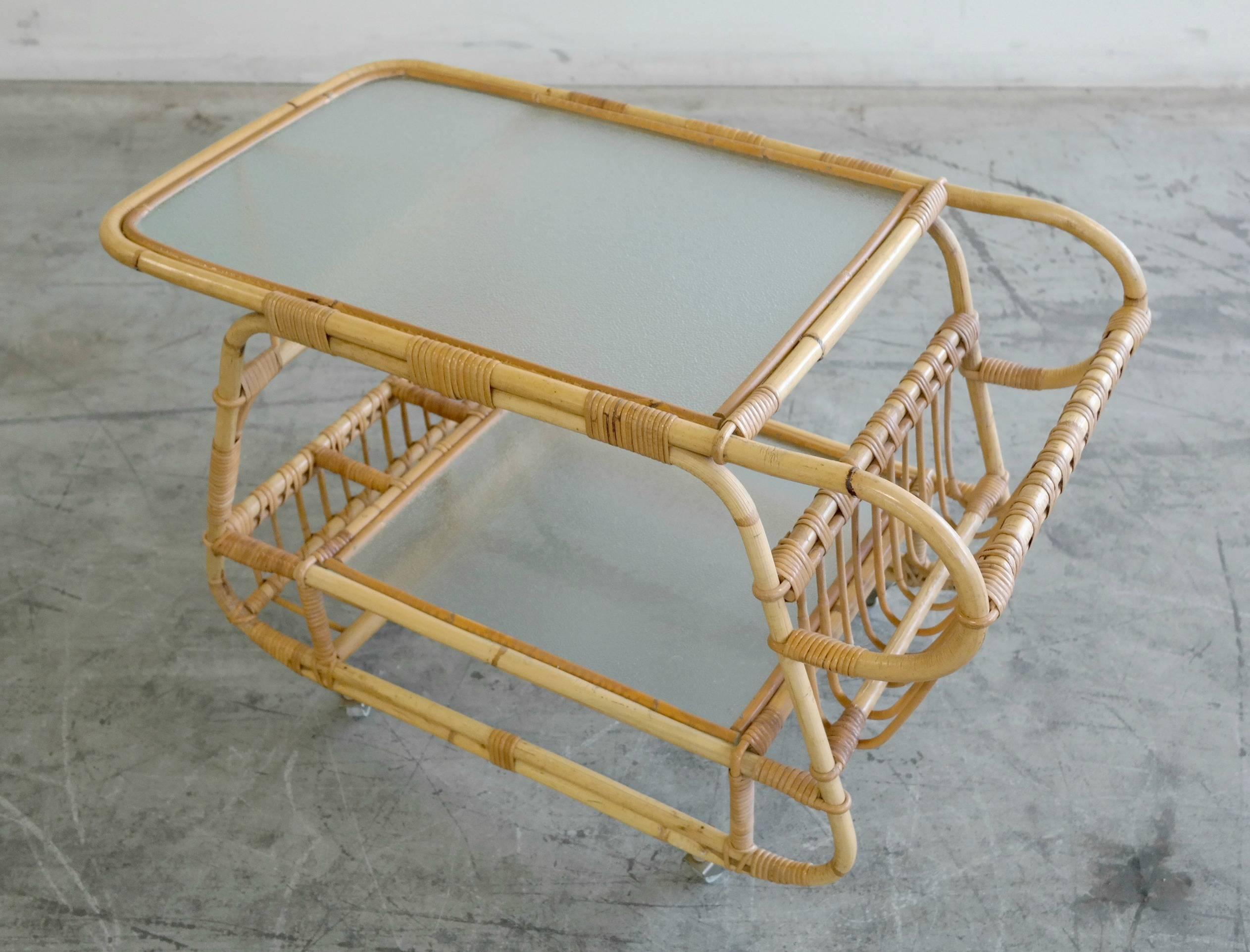 This is a beautiful Mid-Century rattan bar cart. Has a rack for magazines and a frosted glass top as well as frosted glass bottom tray and extra compartments for additional storage. Great design and style. In great shape with no cracks on the glass.