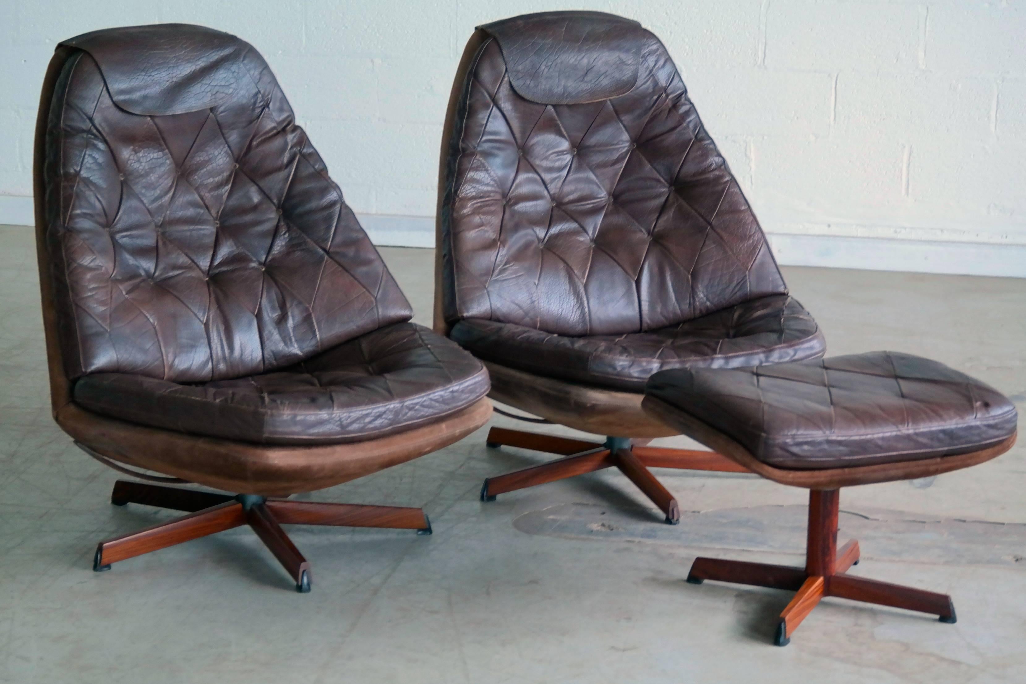 Pair of 1960s Danish leather swivel chairs with one matching ottoman and neck covers. These are simply some of the most scrumptious leather swivel chairs ever made. Top grain supple chocolate colored leather resting on a base covered in cognac