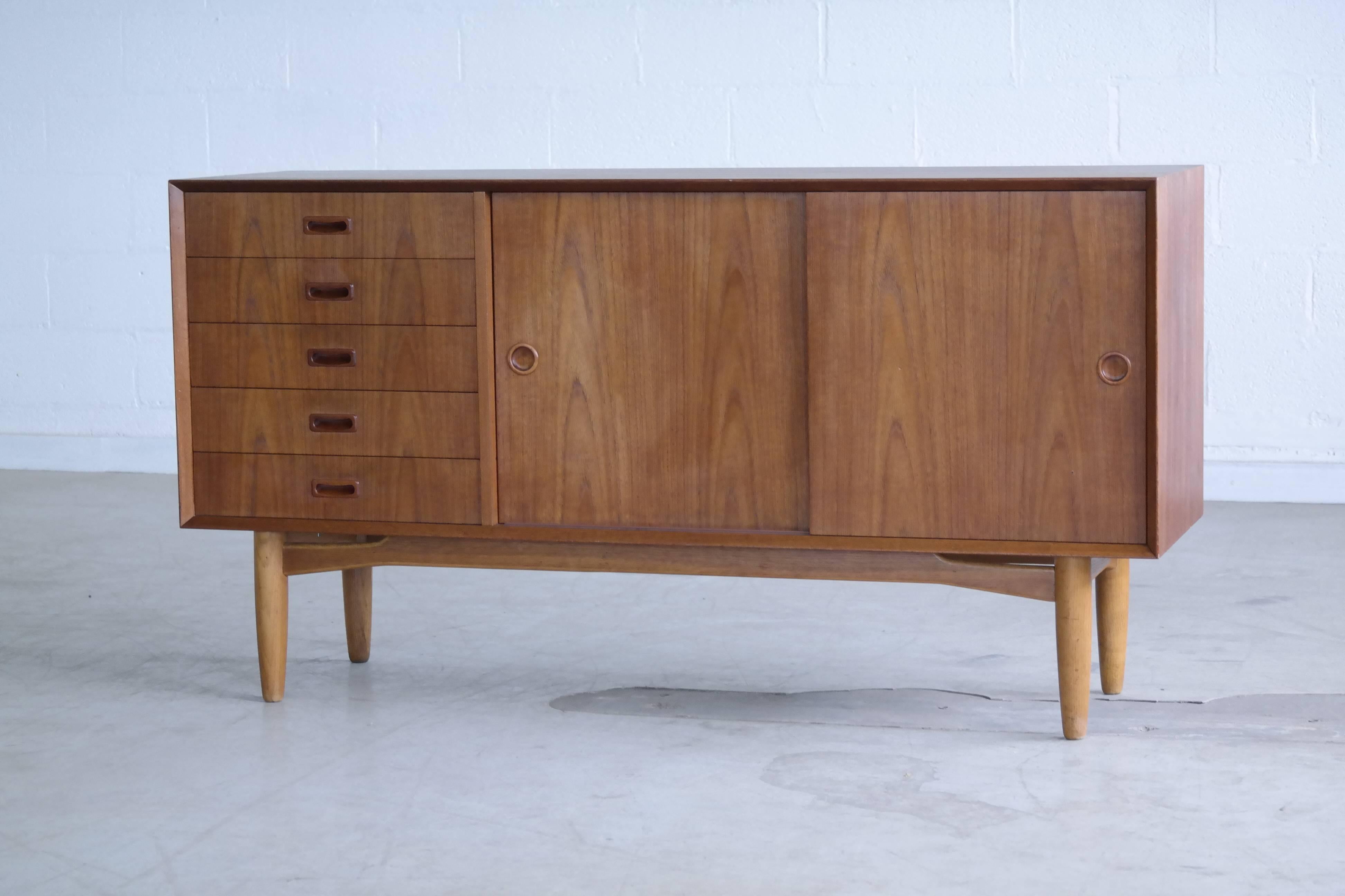 Mid century classic Omann Jun design and quality. This Low teak credenza with carved pulls on a base of solid oak provides lots of storage space and packs a punch for its size.