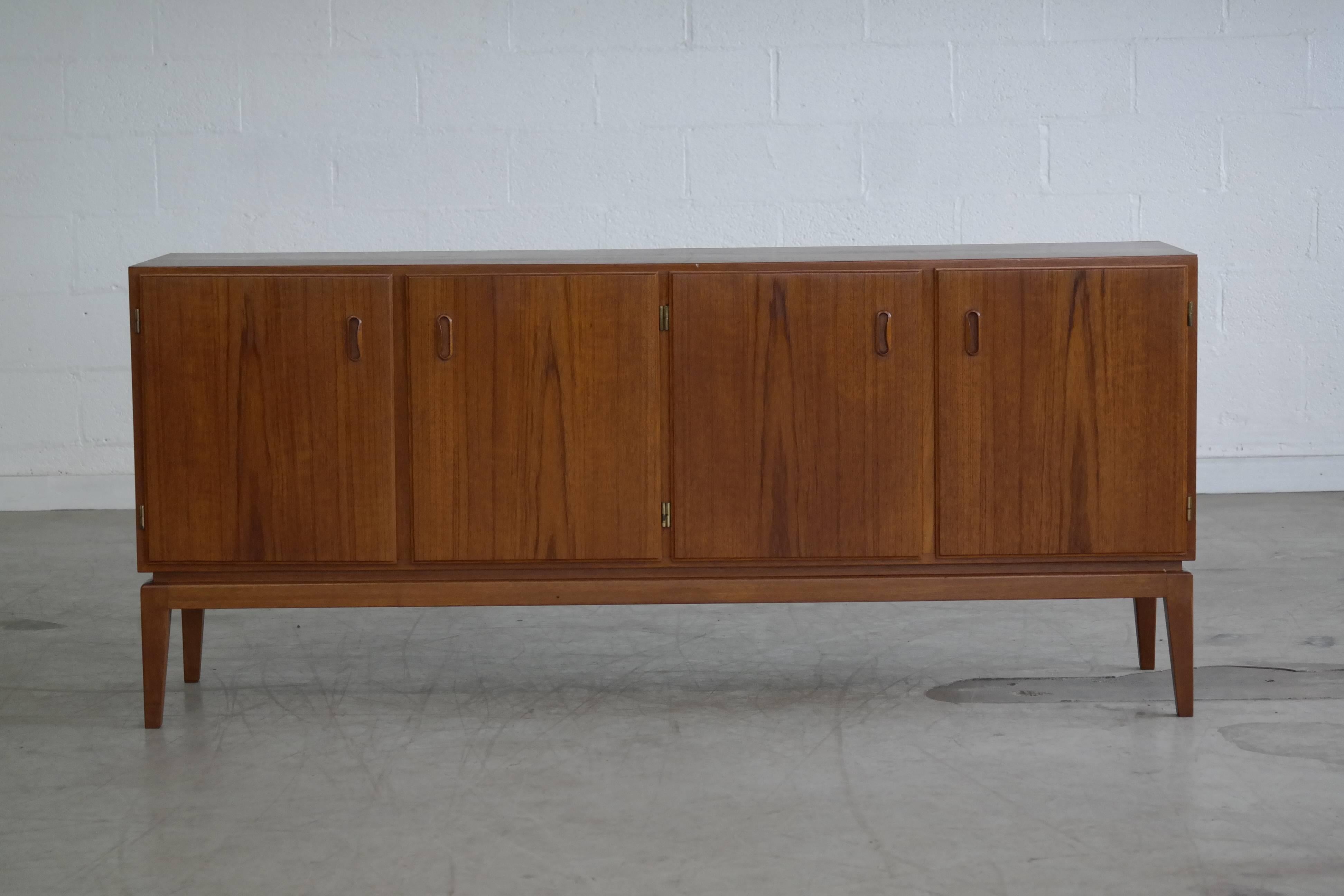 Beautifully proportioned low teak credenza with clean lines in excellent condition. Four compartments each with one adjustable shelf. Very nice grain figure and color.
 