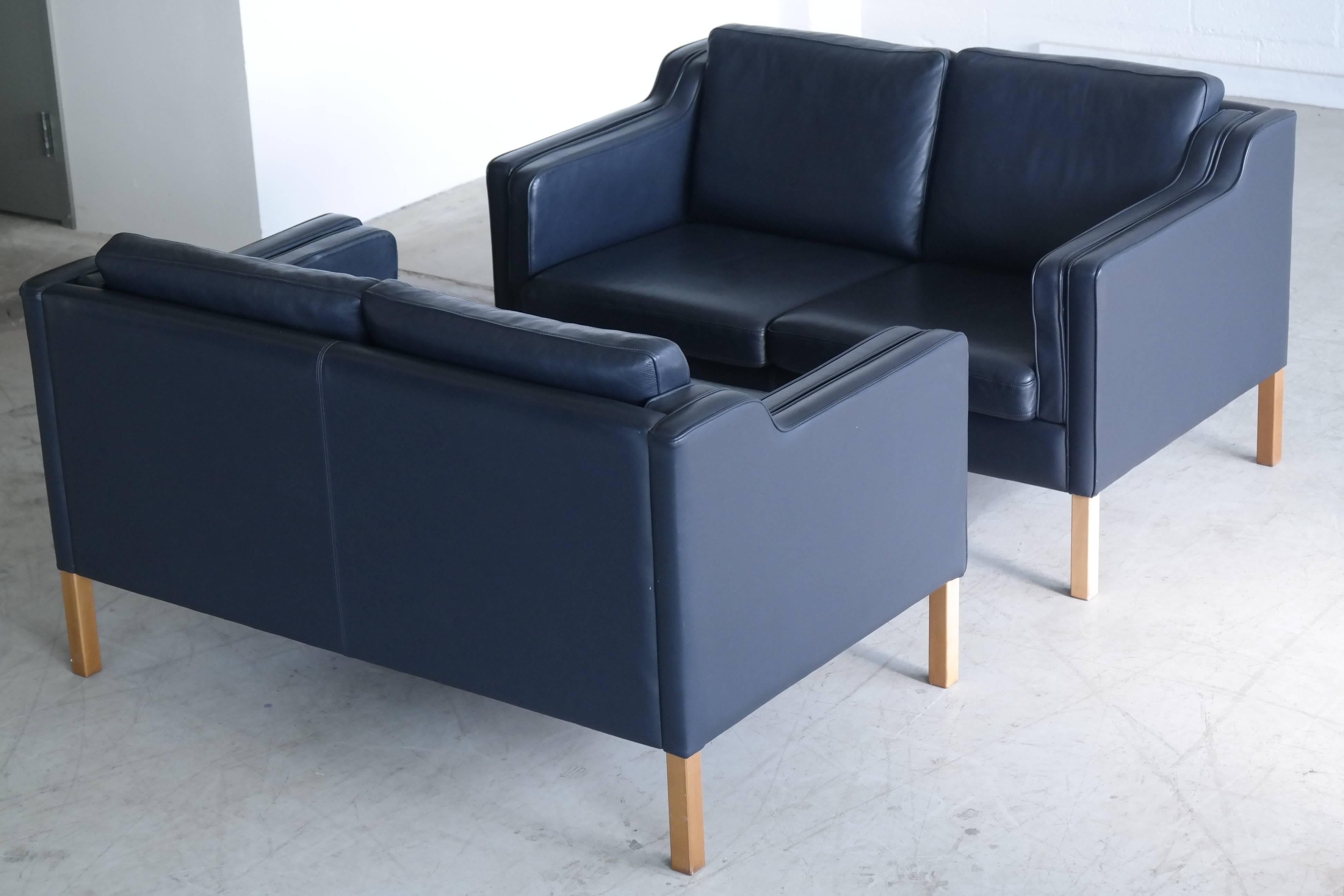 Very elegant and comfortable classic pair of Borge Mogensen style sofas model 2212 in dark sapphire navy blue leather by Stouby Polsterfabrik of Denmark. High quality leather over a beech wood frame and legs. Nicely worn in cushions are top filled