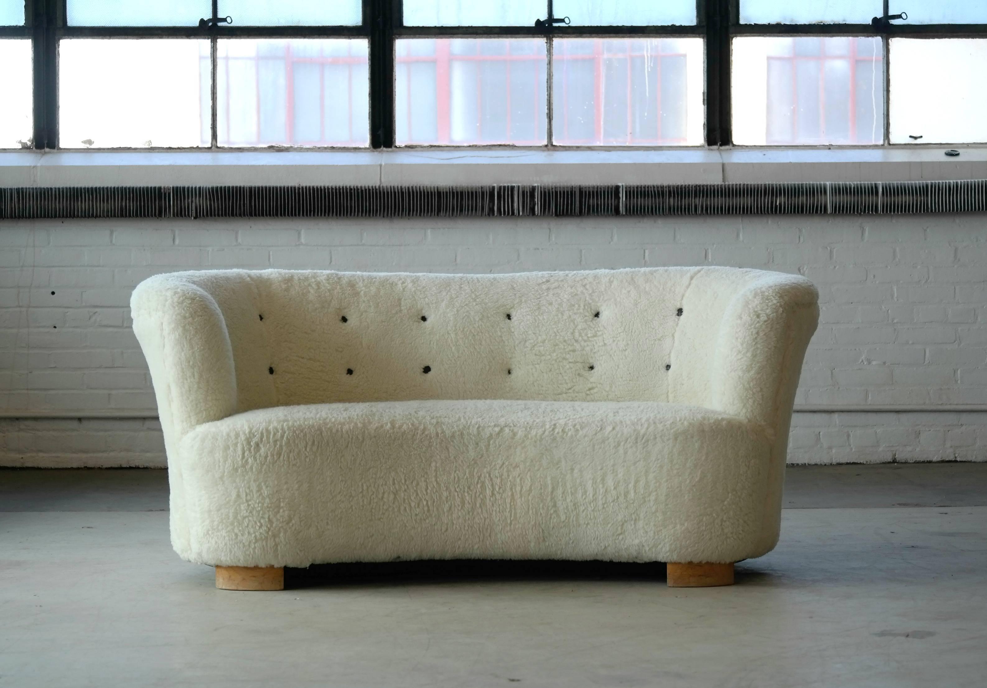 Banana shaped loveseat sofa reupholstered in faux lambs fur with cognac brown leather buttons, made by Slagelse Møbelværk in the 1940s. This sofa will make strong statement in any room. Beautiful round lines and iconic block feet. Fully refurbished