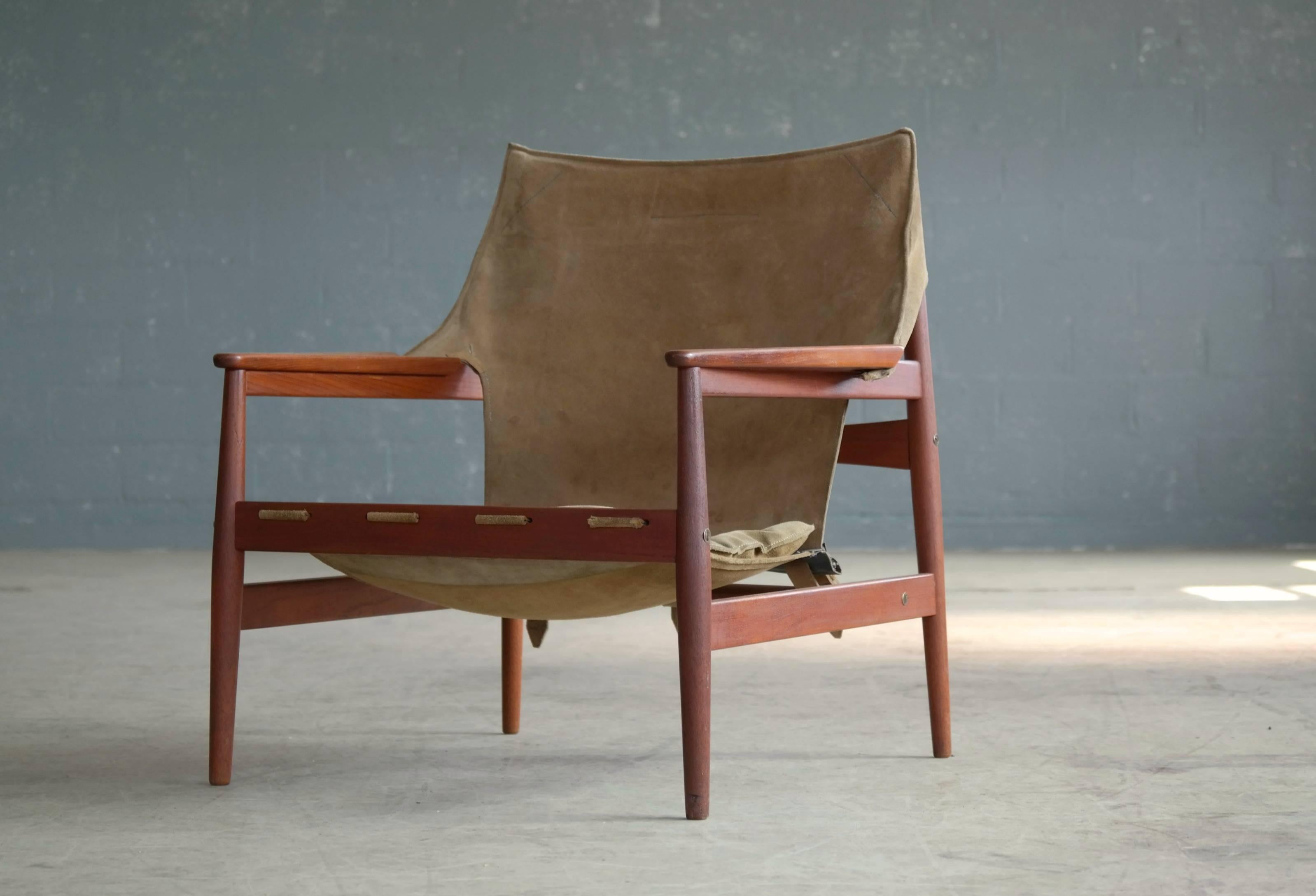 Spectacular 1960s sling safari chair by Hans Olsen for Viskadalens Mo¨belfabrik AB, Sweden. Tan suede sling with three-buckle support fitted over a beautiful contoured solid teak frame with carved armrests. Lightly cushioned seat. 

Both the suede