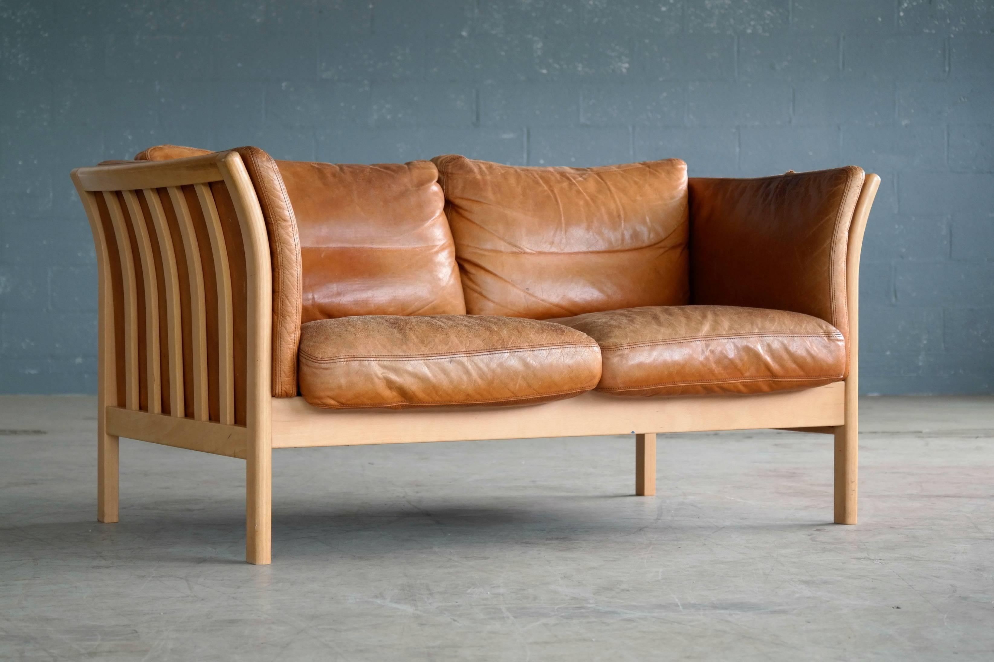 Very nice Danish 1960s two-seat with cognac colored leather and traditional Scandinavian blond beechwood frame with spokes on the sides in the style of Børge Mogensen. Admirable patina and wear with some crazing to the top of the armrests and a