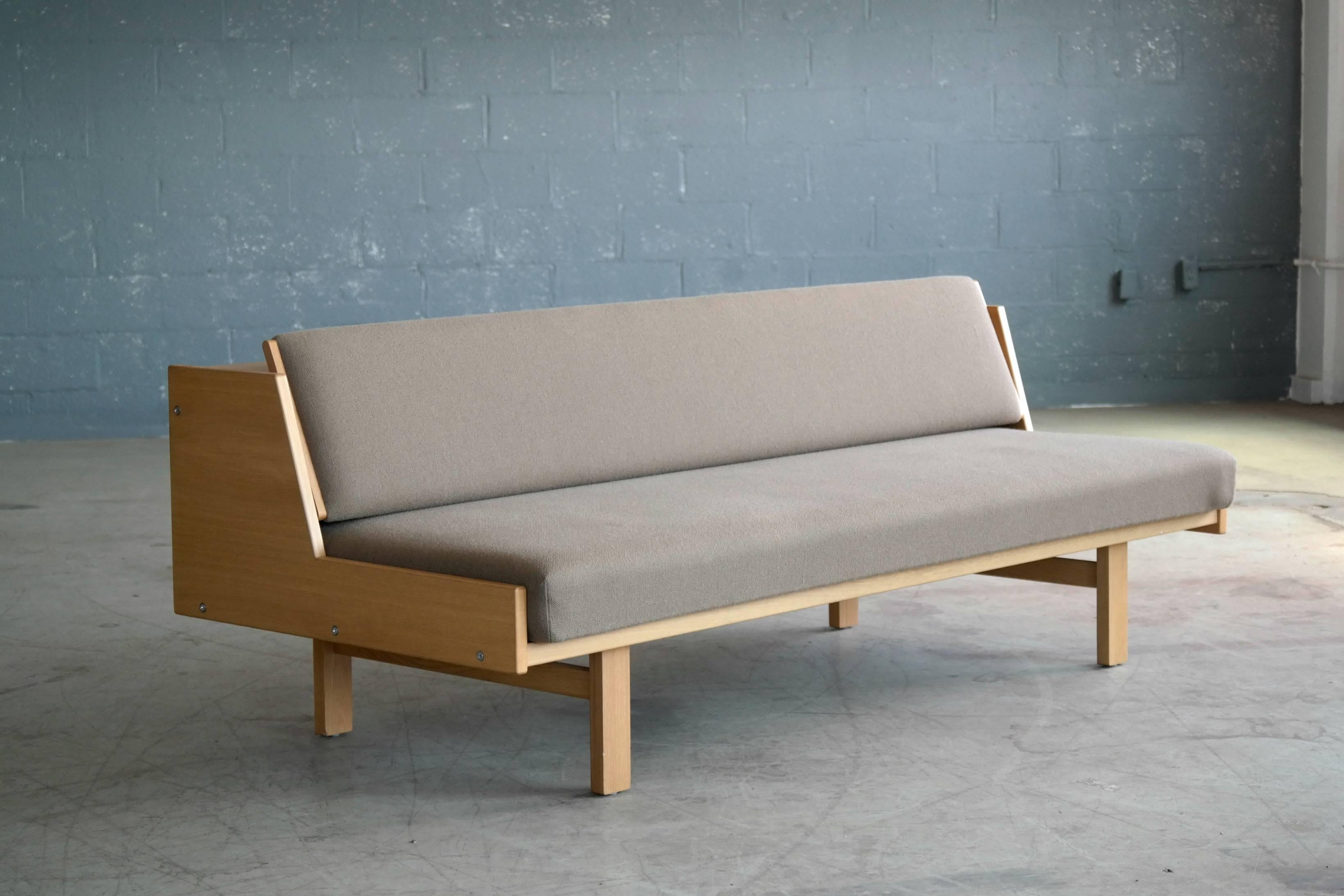 Hans Wegner's iconic daybed designed in 1954 and produced by GETAMA in Denmark. The daybed is made from oak and has it's original mattress covered in a grey wool by Kvadrat. The backrest which also serves as blanket storage lifts up to allow the
