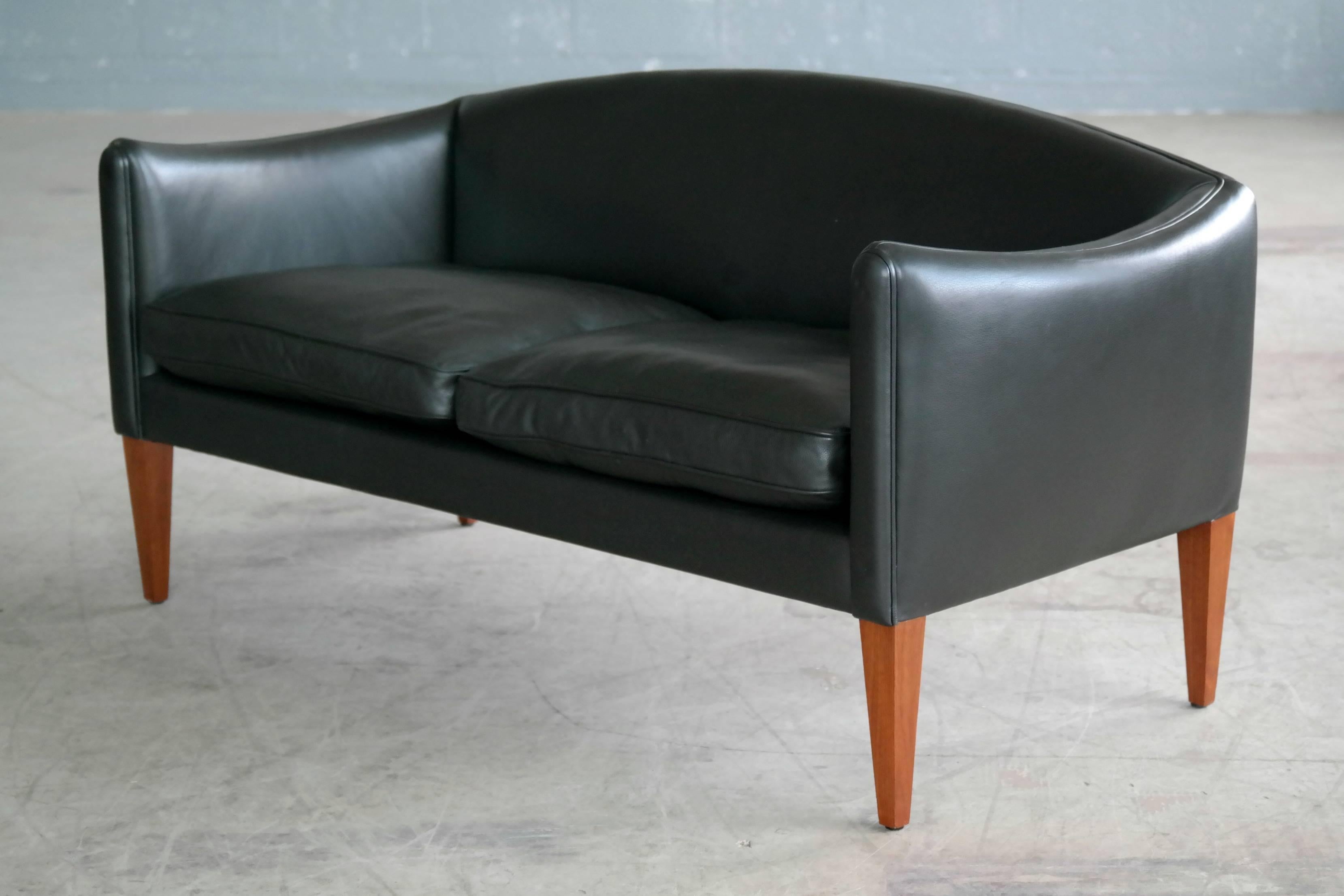 Exuberant sought after Illum Wikkelsø 1960s two-seat sofa or settee for Holger Christiansen in supple black leather and solid teak legs. Minimal age wear excellent overall condition.