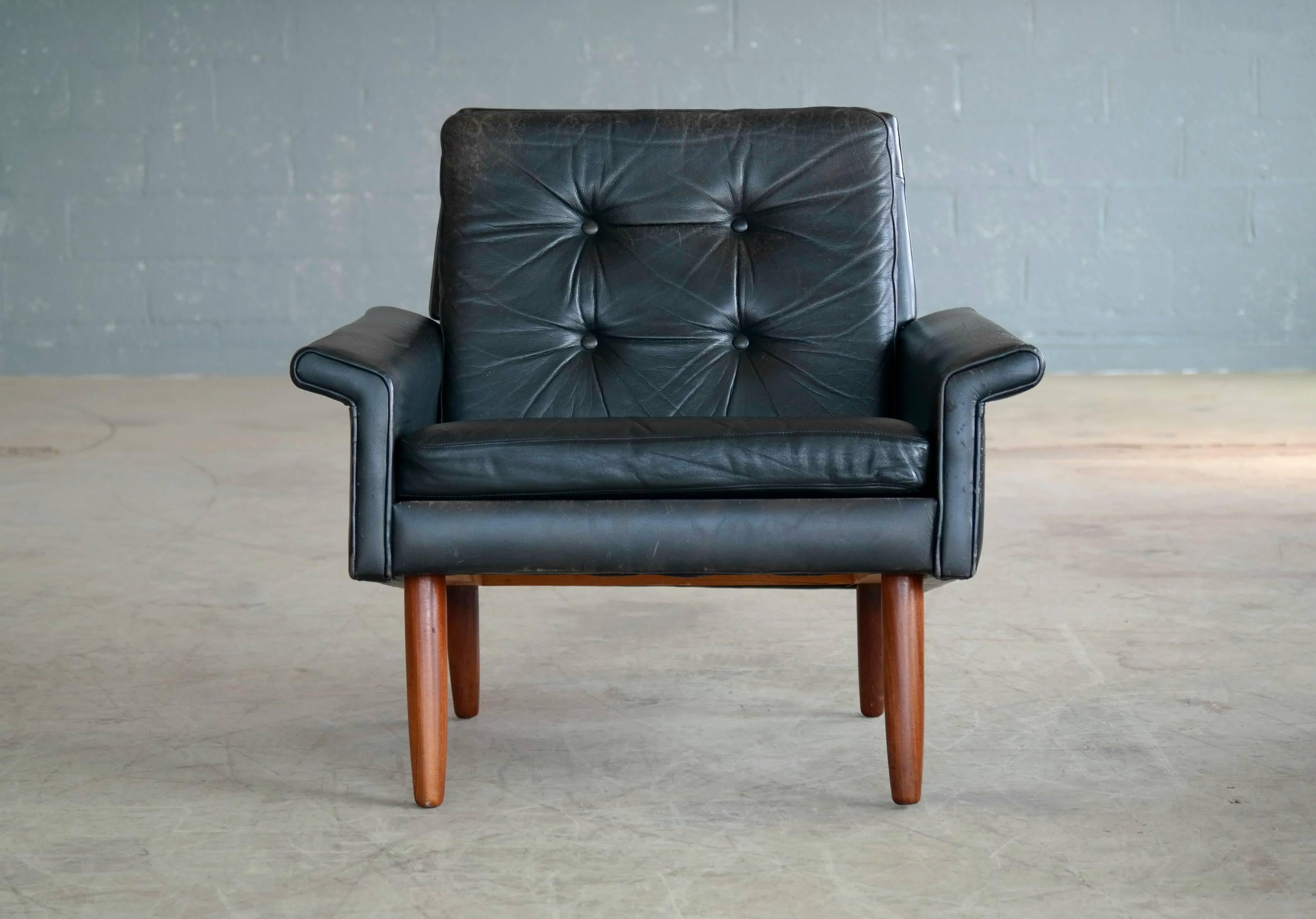 Illum Wikkelsø style easy chair in black leather and solid teak legs made in Denmark, late 1960s. Nice worn in patina with some scuffs and scratches. Very good condition overall.