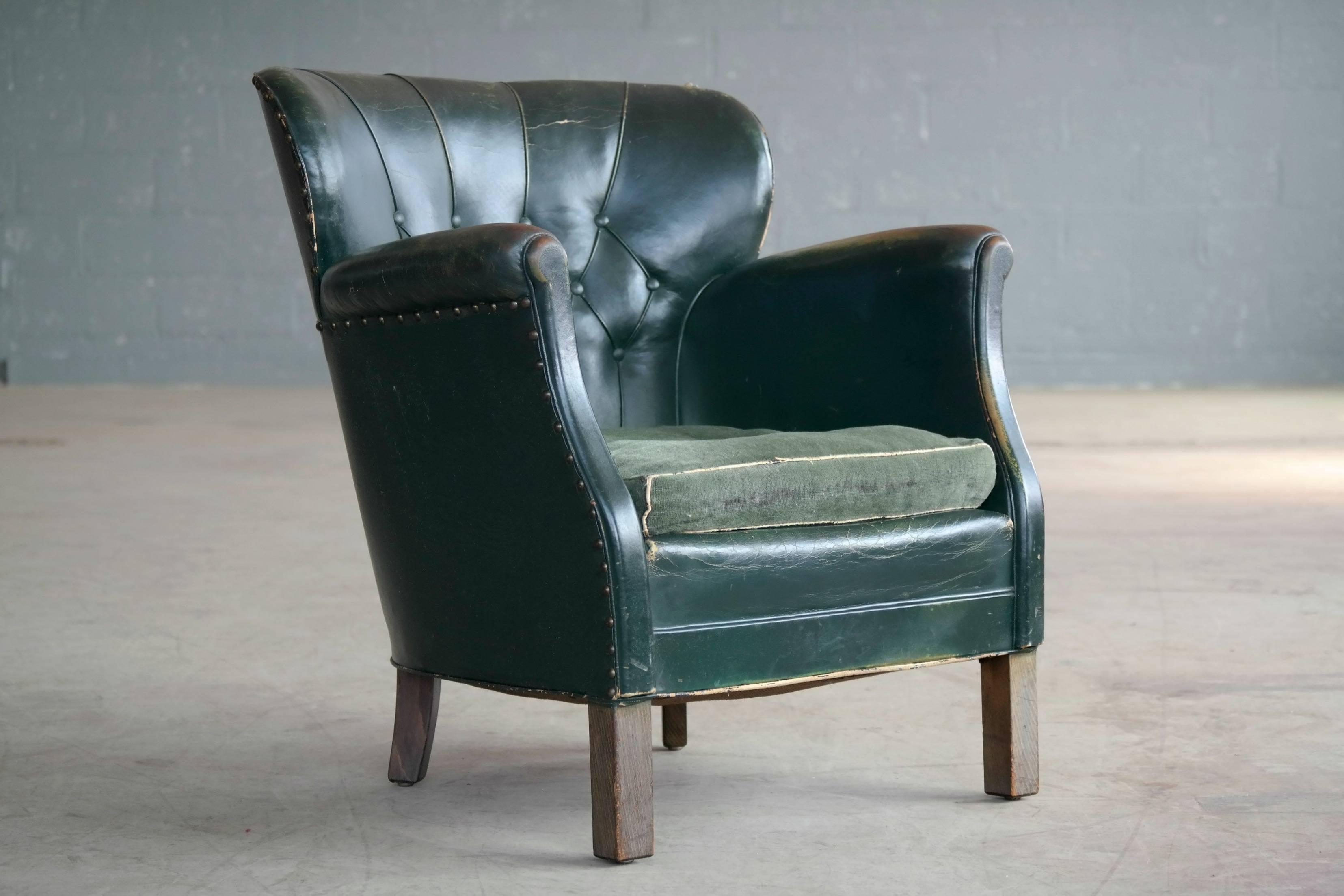 A Classic Danish small-scale club chair from the post Art Deco period of the late 1930s. Fantastic patinated original green leather with a buttoned back and brass tacks. Later added green velvet cushion. Noble patina and wear to especially the
