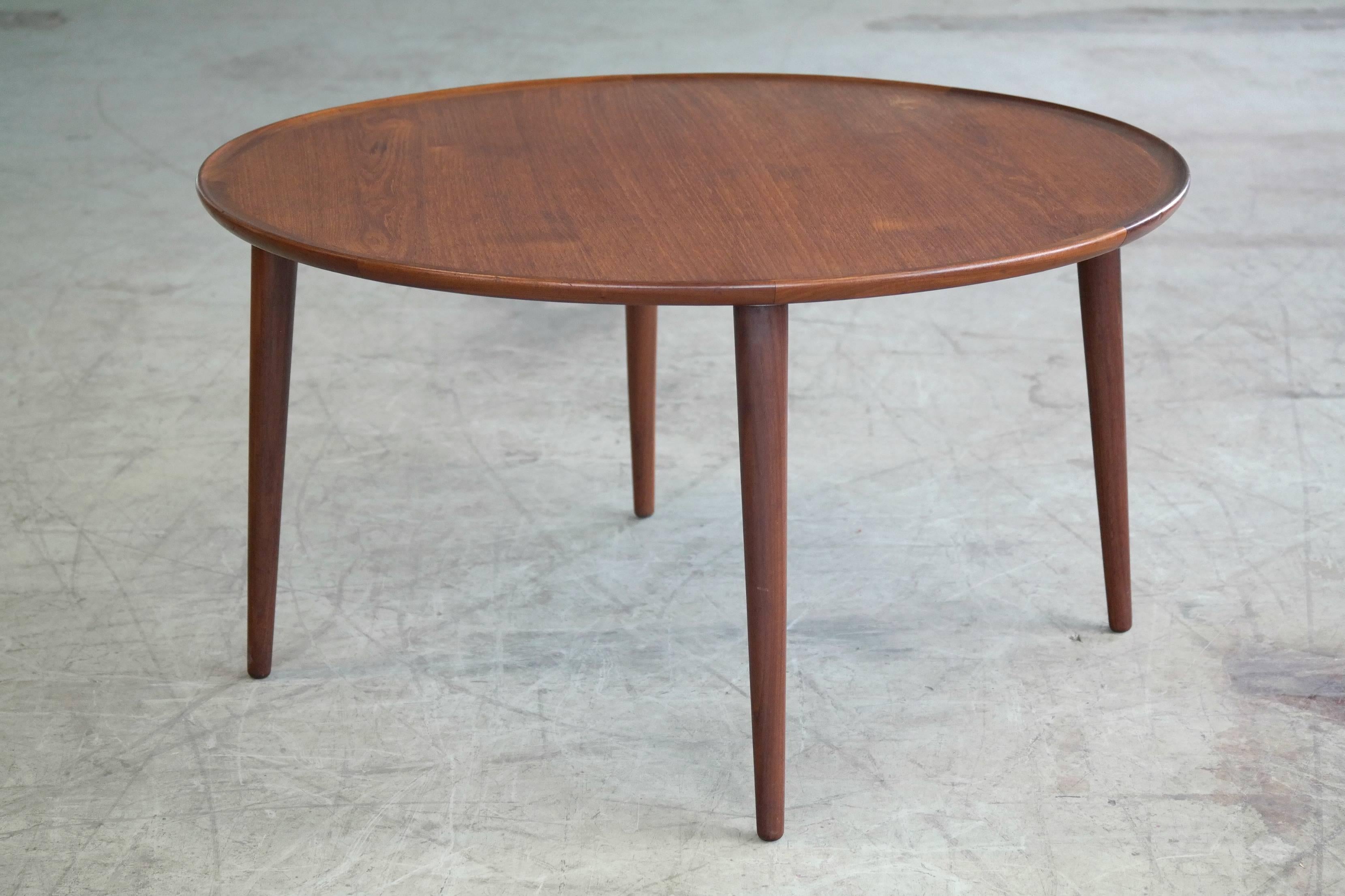 Beautiful teak coffee table by Peter Hvidt. Round top with nice solid teak lip resting on four tapered solid teak splayed legs. Pure elegance and overall excellent condition.