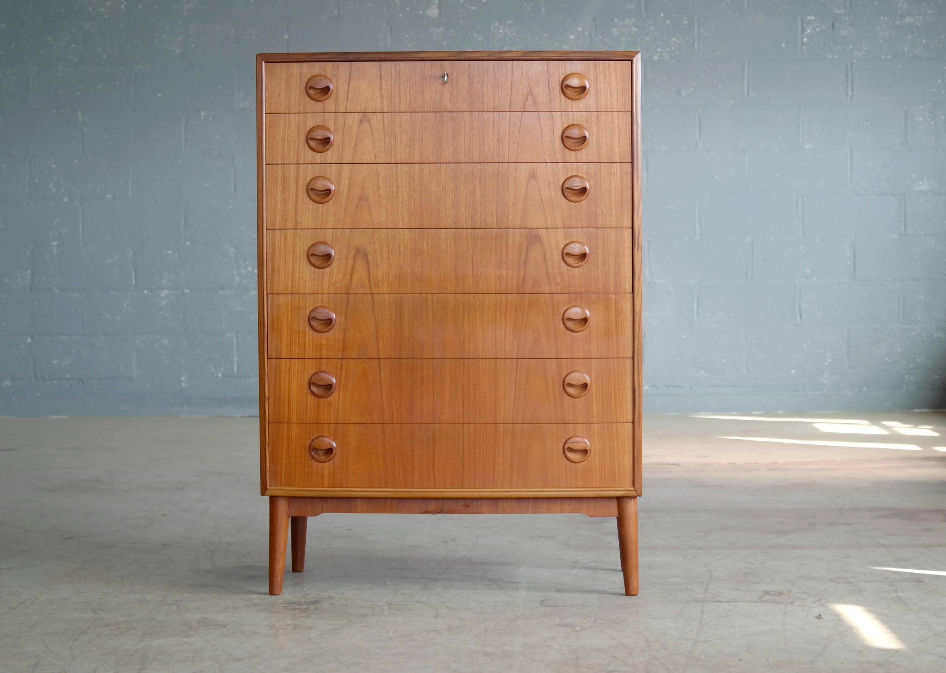 Beautiful Danish teak high-boy dresser or chest of drawers designed by Kai Kristiansen in the 1950s. Teak veneer with edges of solid teak and pulls carved from solid teak raised on solid tapered teak legs. All drawers solid ply. Locking top drawer