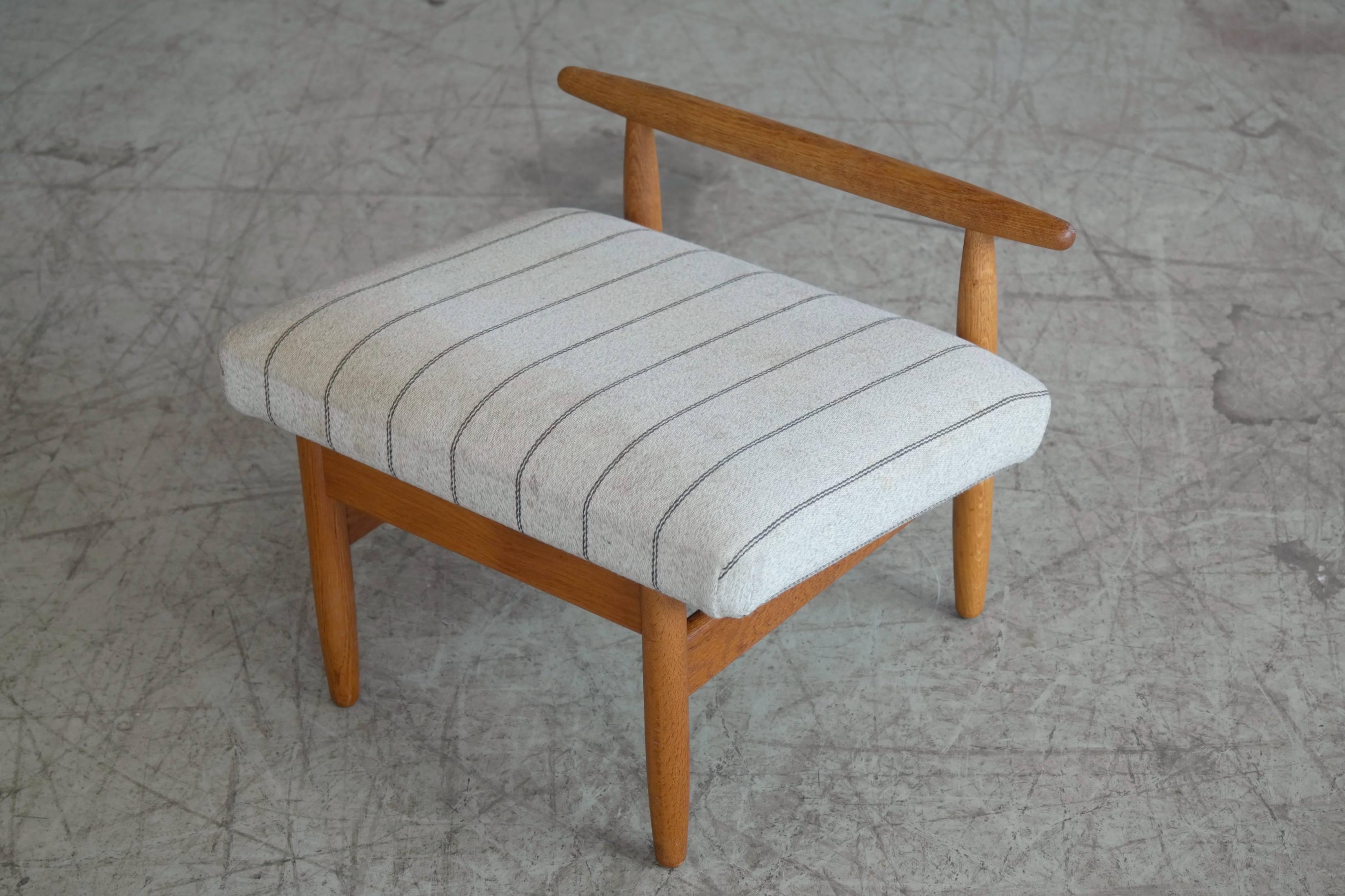 Elegant footstool model J65 designed by Ejvind Johansson in 1956 for FDB Mobler, Denmark. Solid oak and original wool fabric. Nice grain and patina to the wood, while the fabric is showing some light soiling and would benefit from being