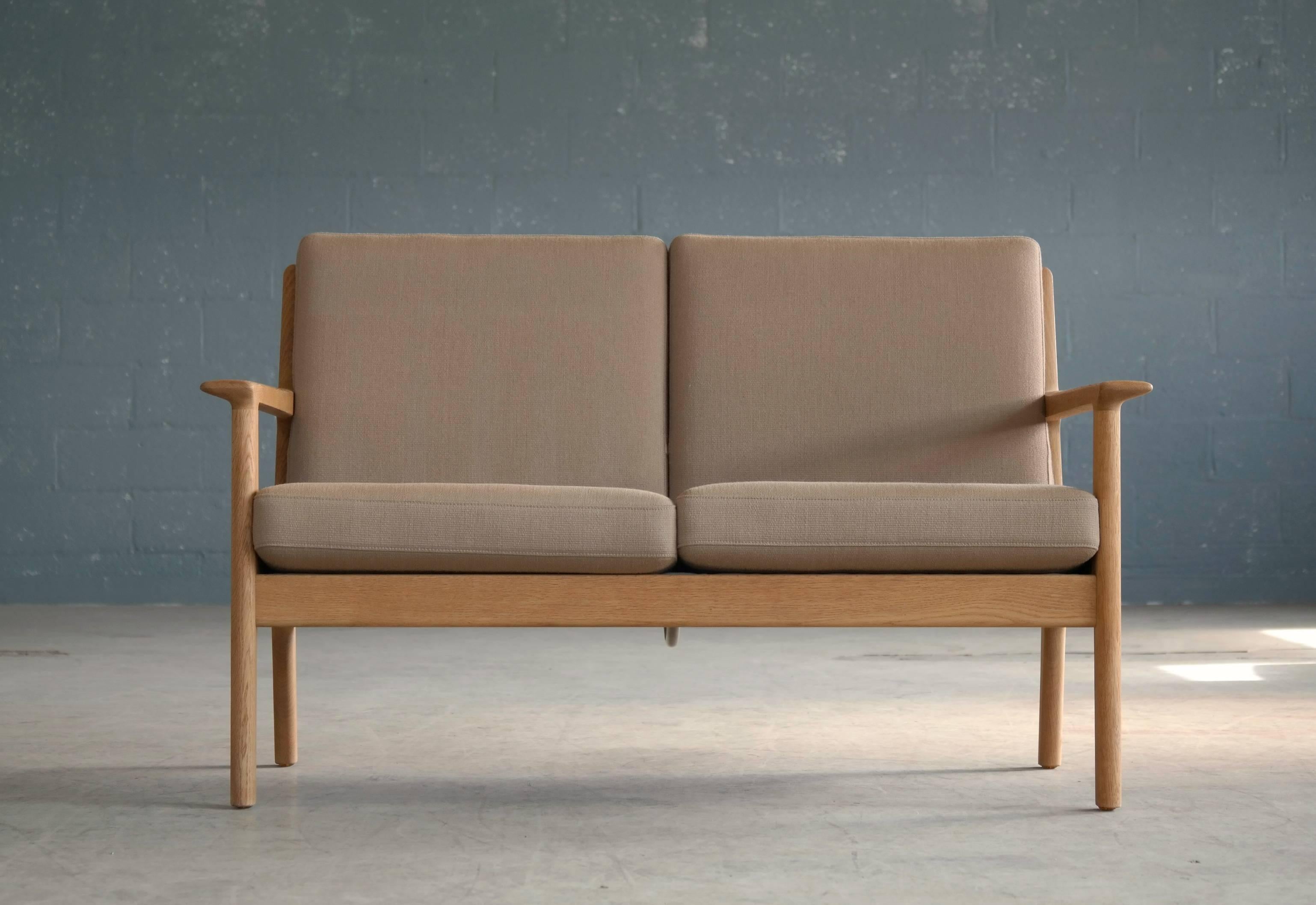The model GE265 two-seat sofa designed by Hans J Wegner for GETAMA in the early 1970s featuring a solid oak frame and wool covered foam cushions. The cushions remain in their original wool. The sofa is in excellent vintage condition with a nice