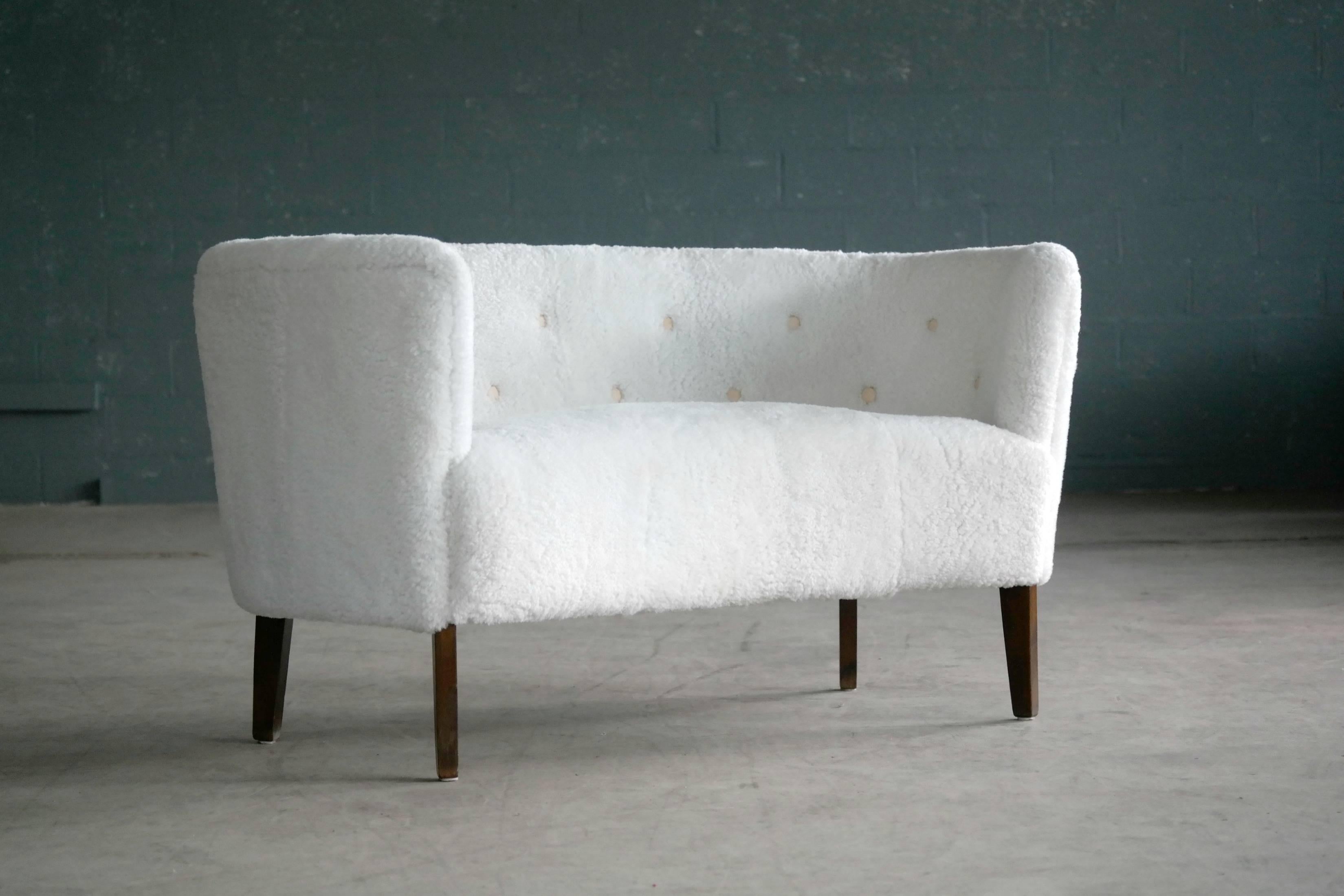 Very sophisticated and stylish petite curved settee in the classic style of Flemming Lassen and Georg Kofoed and also bearing resemblance to some of Finn Juhl's popular designs. Upholstered in white lambsfur with leather buttons, raised on stained
