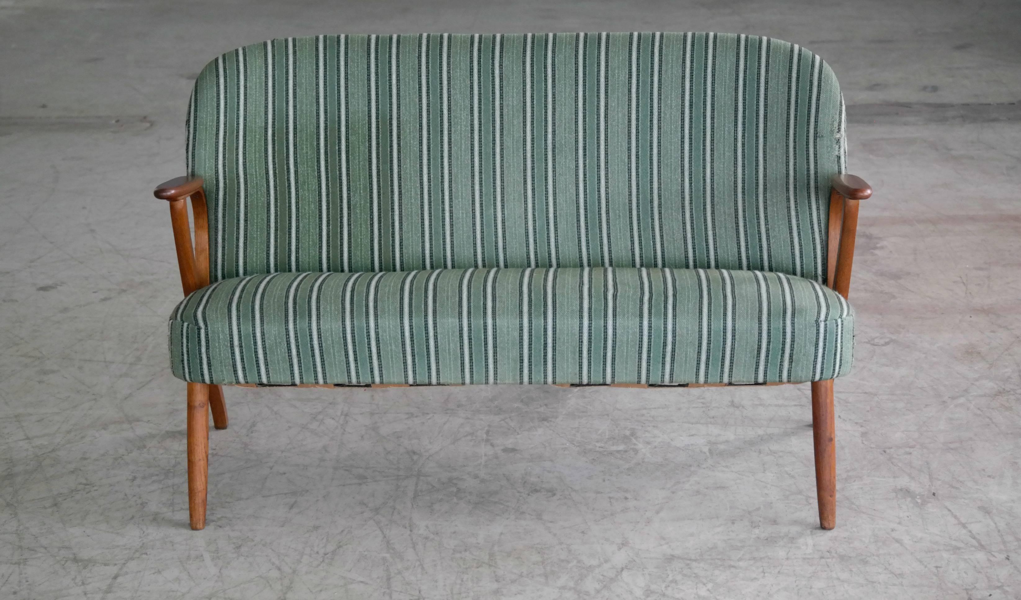 Beautiful and elegant small 1950s Danish sofa with legs and armrests in teak. The high quality woodwork and design is very much in the style of Kurt Olsen and N.A. Jorgensen (Bramin Mobler) but it is unmarked and a rare piece and we cannot be