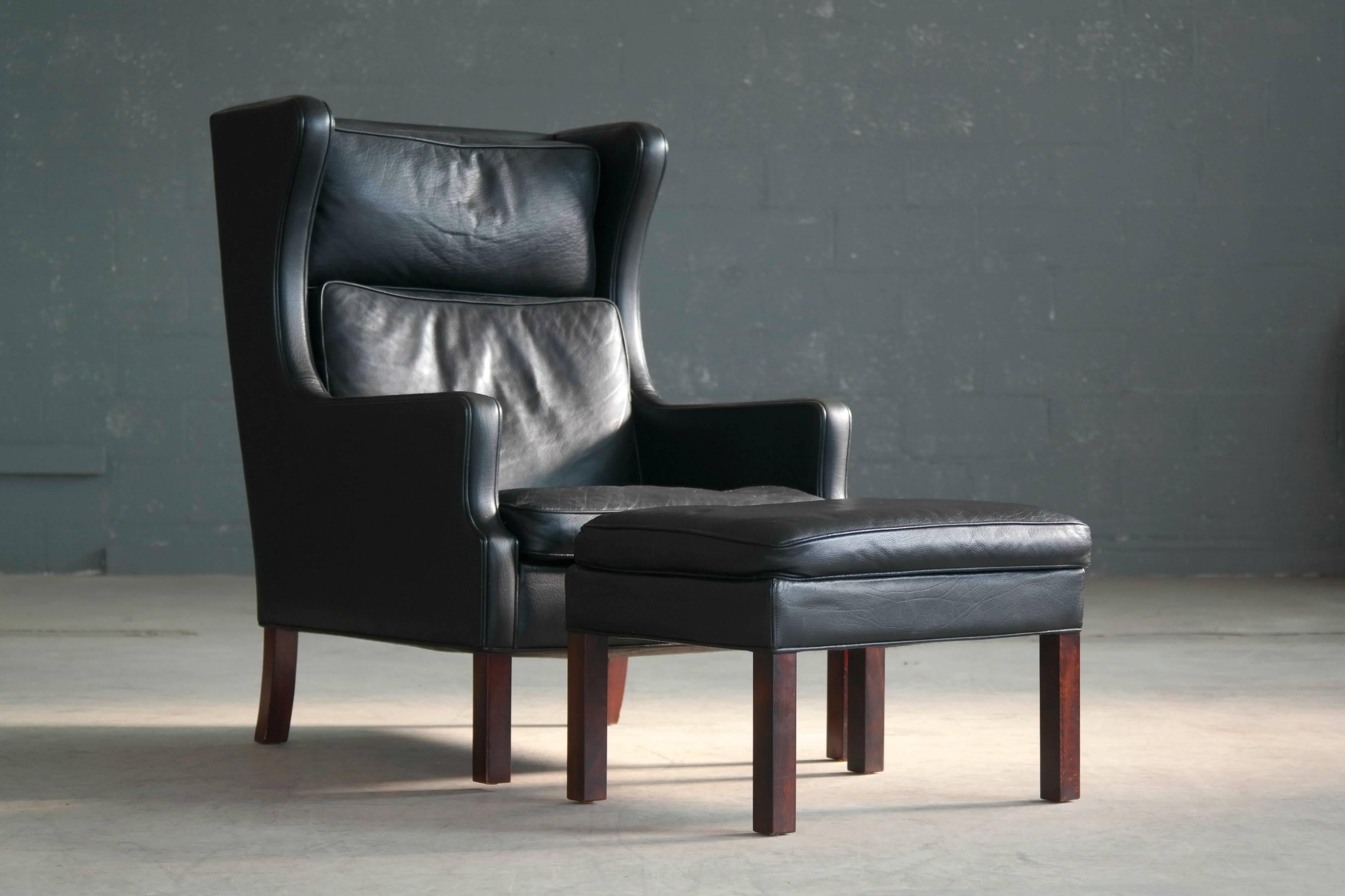 Classic Borge Mogensen style high back lounge chair with ottoman in black leather attributed to Georg Thams and Vejen Polstermobelfabrik, Denmark. Very nice quality leather with great patina and age wear including a little bit of color fading on the