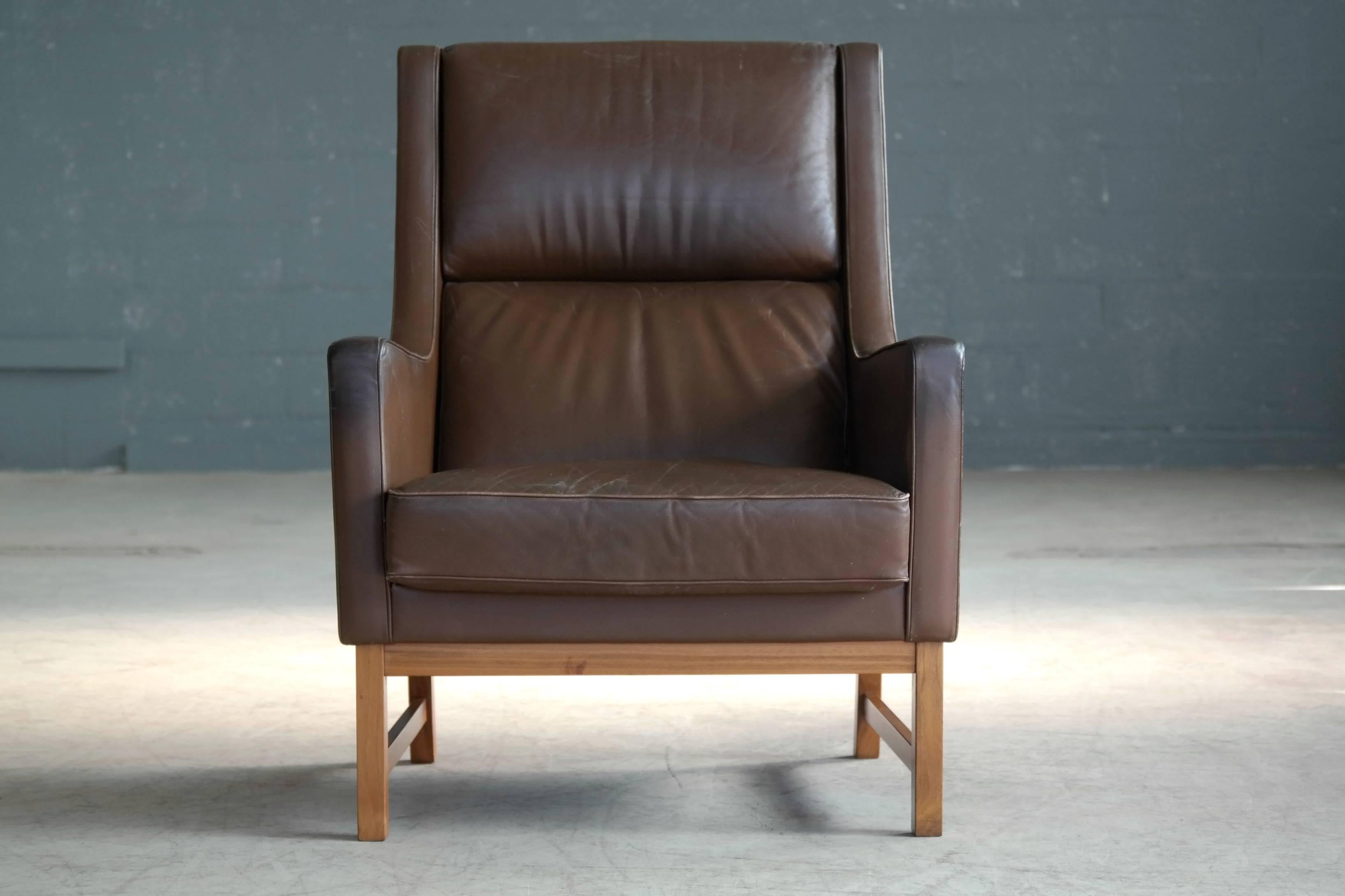 Very elegant Kai Lyngfeldt Larsen style 1960s high back lounge or armchair made in Denmark. Very similar to Larsen's well known but rare designs carried out by Soren WIlladsen. Supple chocolate brown leather raised on a bases of stained beechwood.
