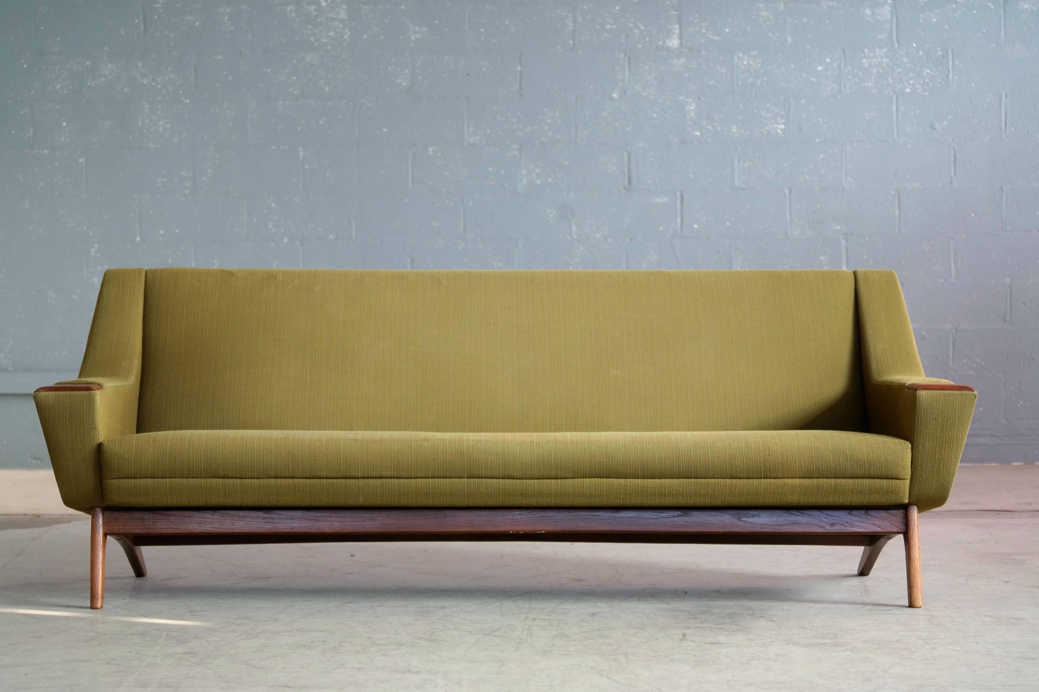 Very elegant and stylish 1960s sofa in the style of Illum Wikkelsø and Leif Hansen for Erhardsen and Erlandsen. Raised on a base and legs of solid teak with large teak accents on the armrests. The base and wood work is in excellent condition while