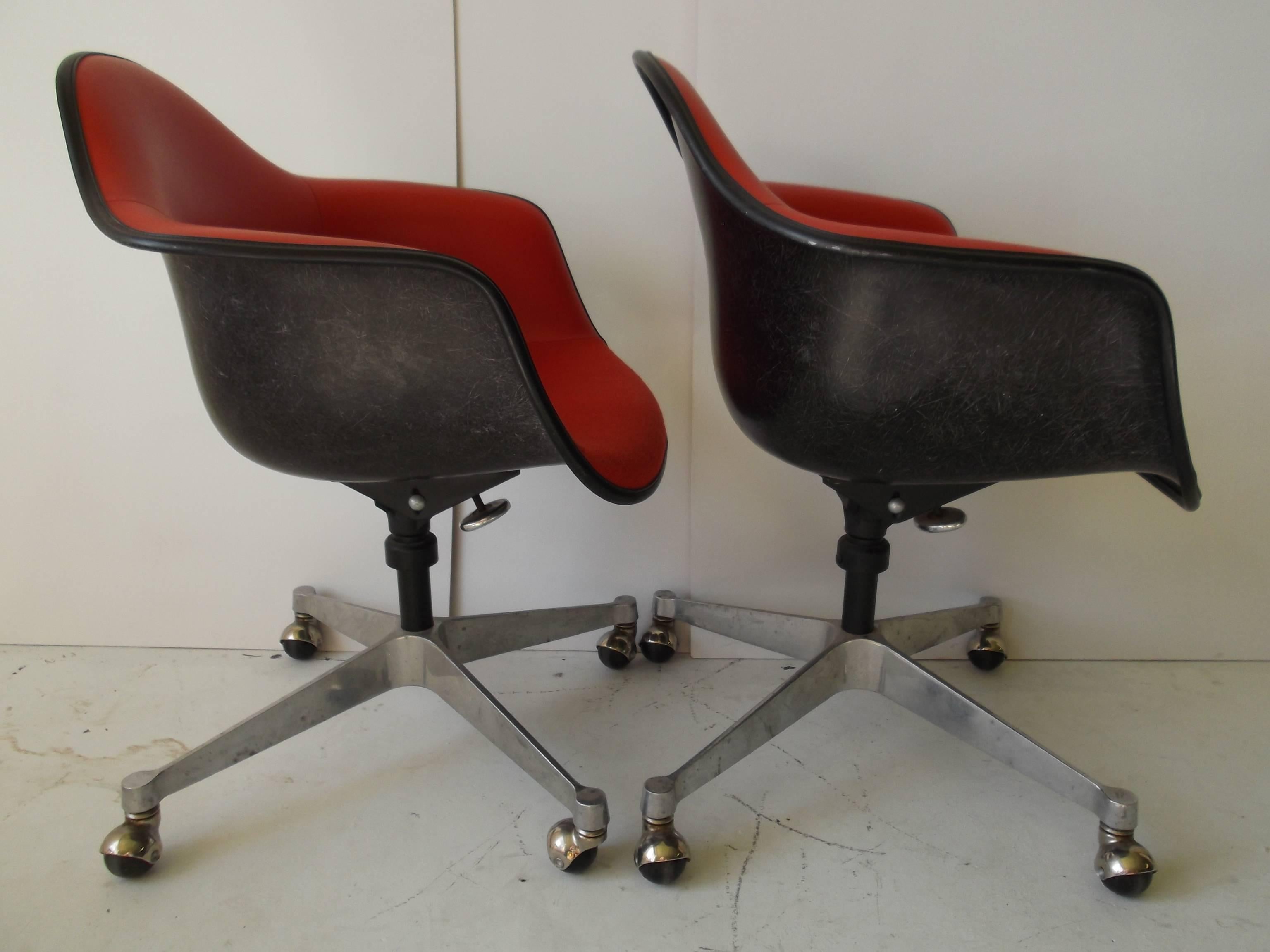 Pair of Herman Miller fiberglass armchairs designed by Charles Eames. They have dated labels to bottom from 1968. There feature red vinyl, and fabric bottom seats, on black fiberglass. Great color combo. You can swivel these to adjust the height,