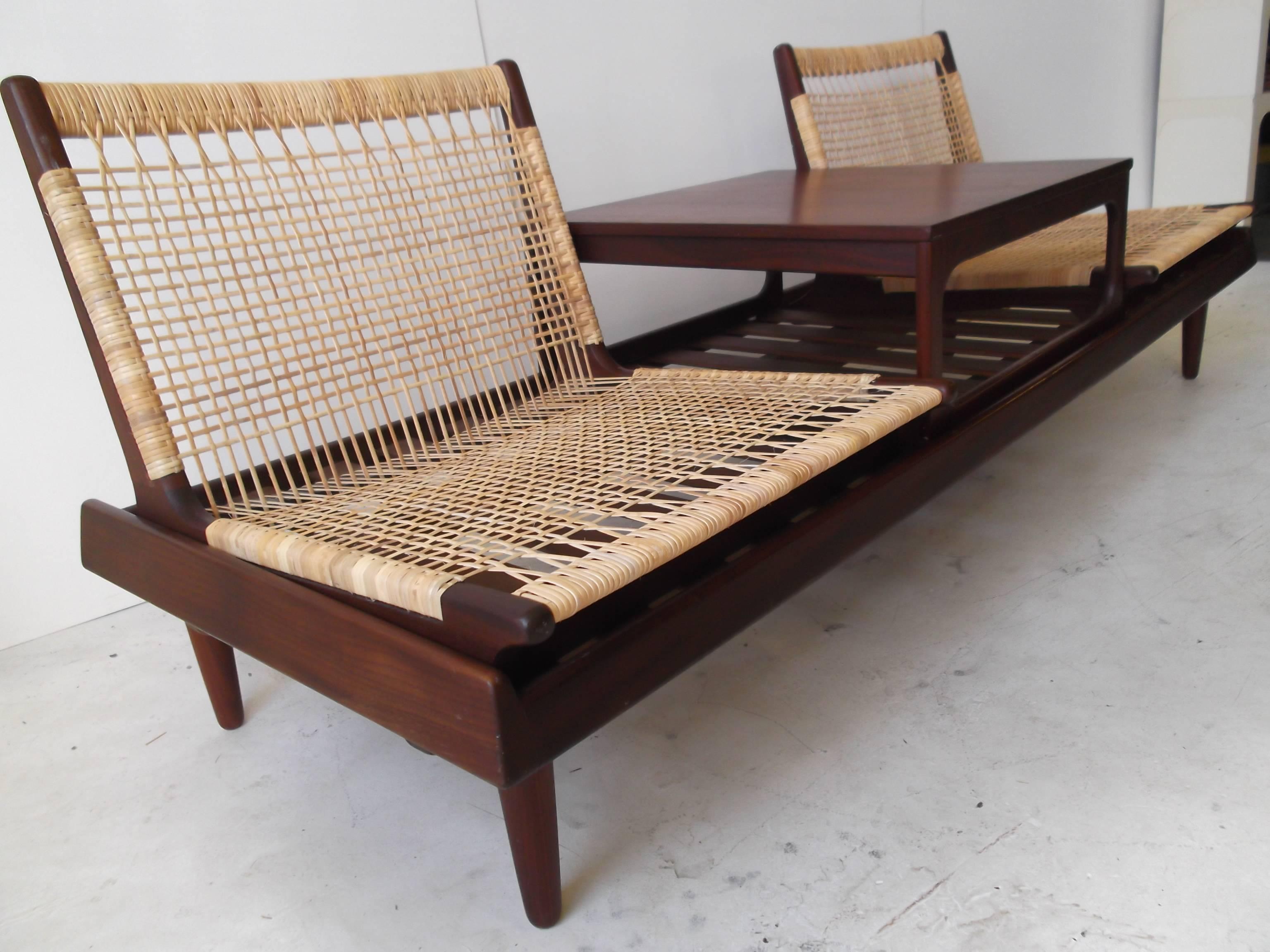 This is a very nice Danish modern sofa by Hans Olsen for Bramin. It is from the 1950s in dark teak. It has two beautifully woven caned seats and a table that rest on a bench. The caning has all been rewoven perfectly. It has orig. heavy foam