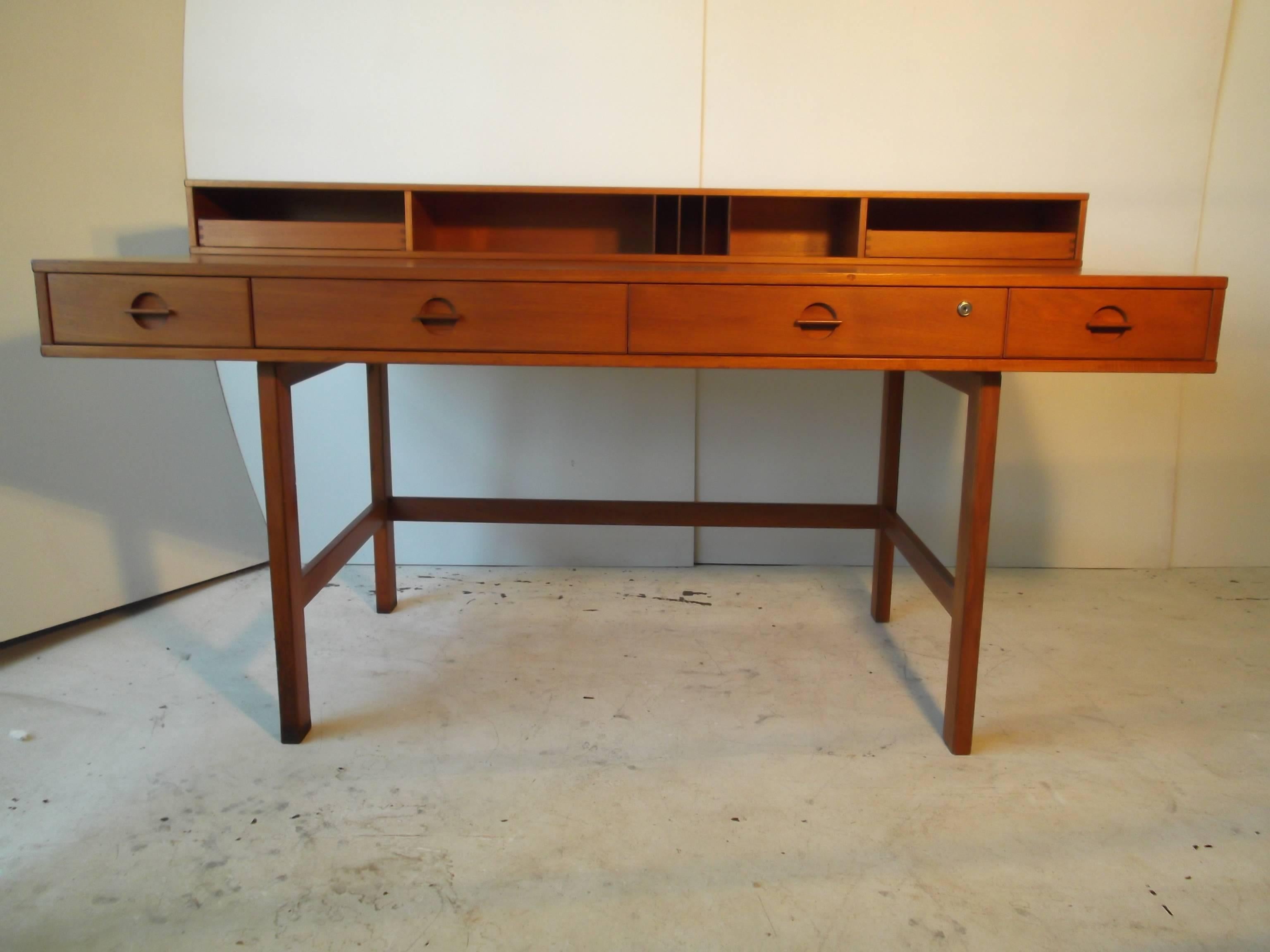 This is a beautiful teak Danish modern desk by Quistgaard for Lovig. It has four drawers across the front with mod handles. There is a cubby hole compartment across the back with two pull-out dovetailed letter trays. The back section flips