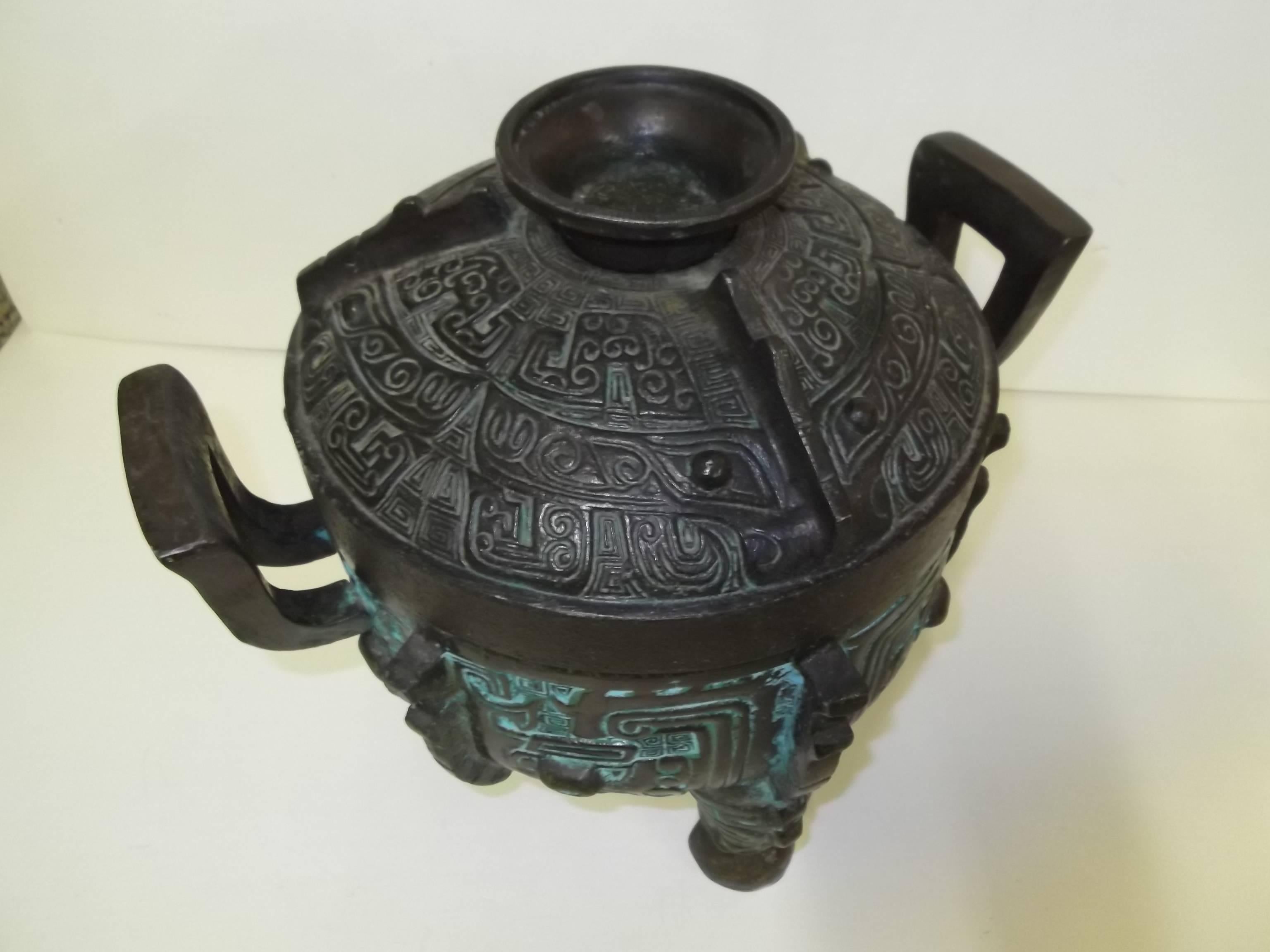 This is a great bar accessory! It is a heavy cast metal ice bucket in the form of an urn or censor, It has deep relief decorating in an Asian design with faces incorporated. It is a dark metal with some green patina accents, less on the lid. It is