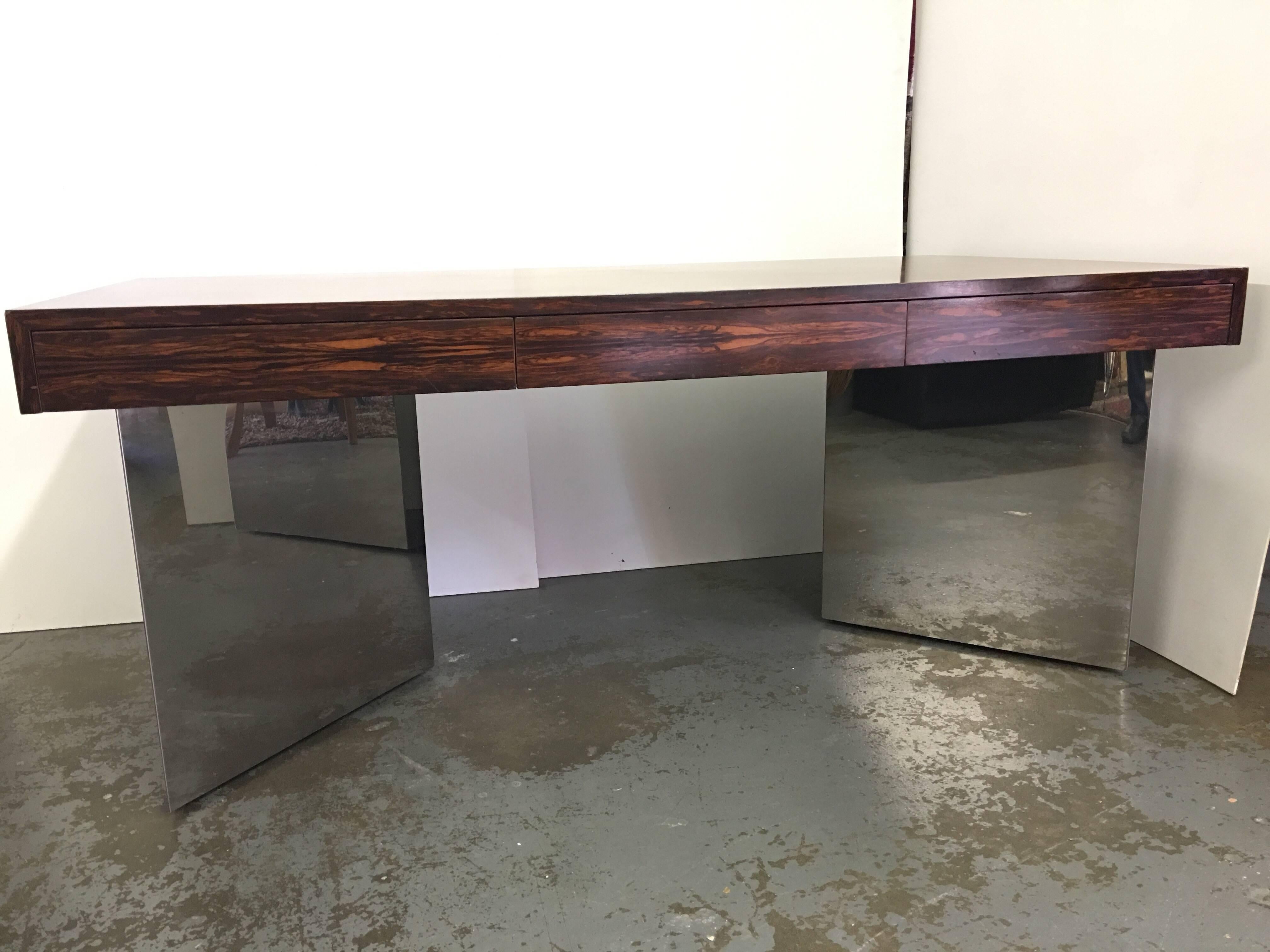 This is an absolute stunner in person. This rosewood desk is attributed to the Pace Collection. The Desk has gorgeous figurale Brazilian Rosewood grain. There are three deep drawers to front. It rests on mirror chrome metal triangular plinths or