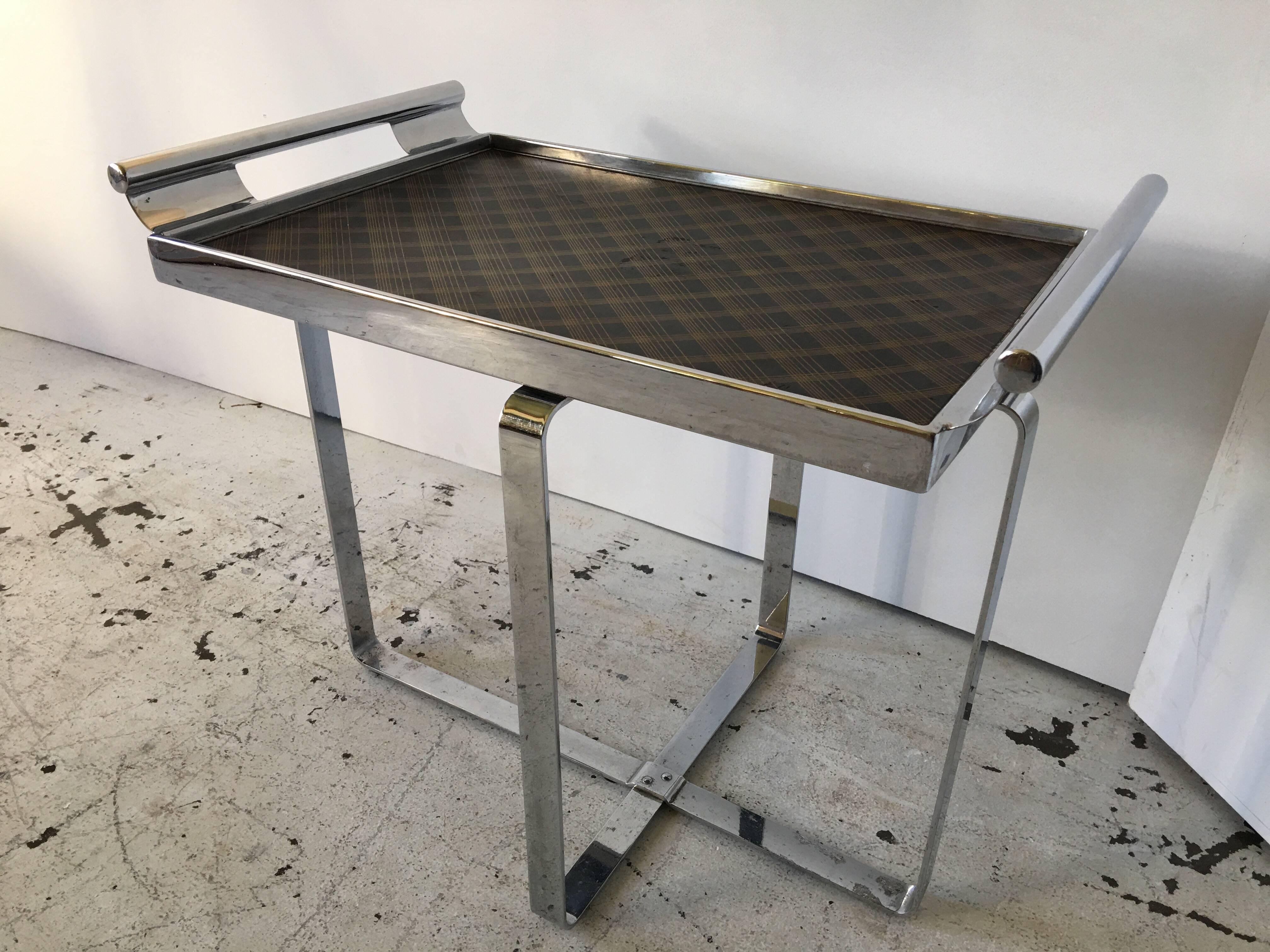 This is an all original flat bar chromed steel, Art Deco table. It features a tight fitting lift off tray for service. The tray has it's original plaid deco like pattern surface. It features and asymmetrical base, that criss-crosses on the floor