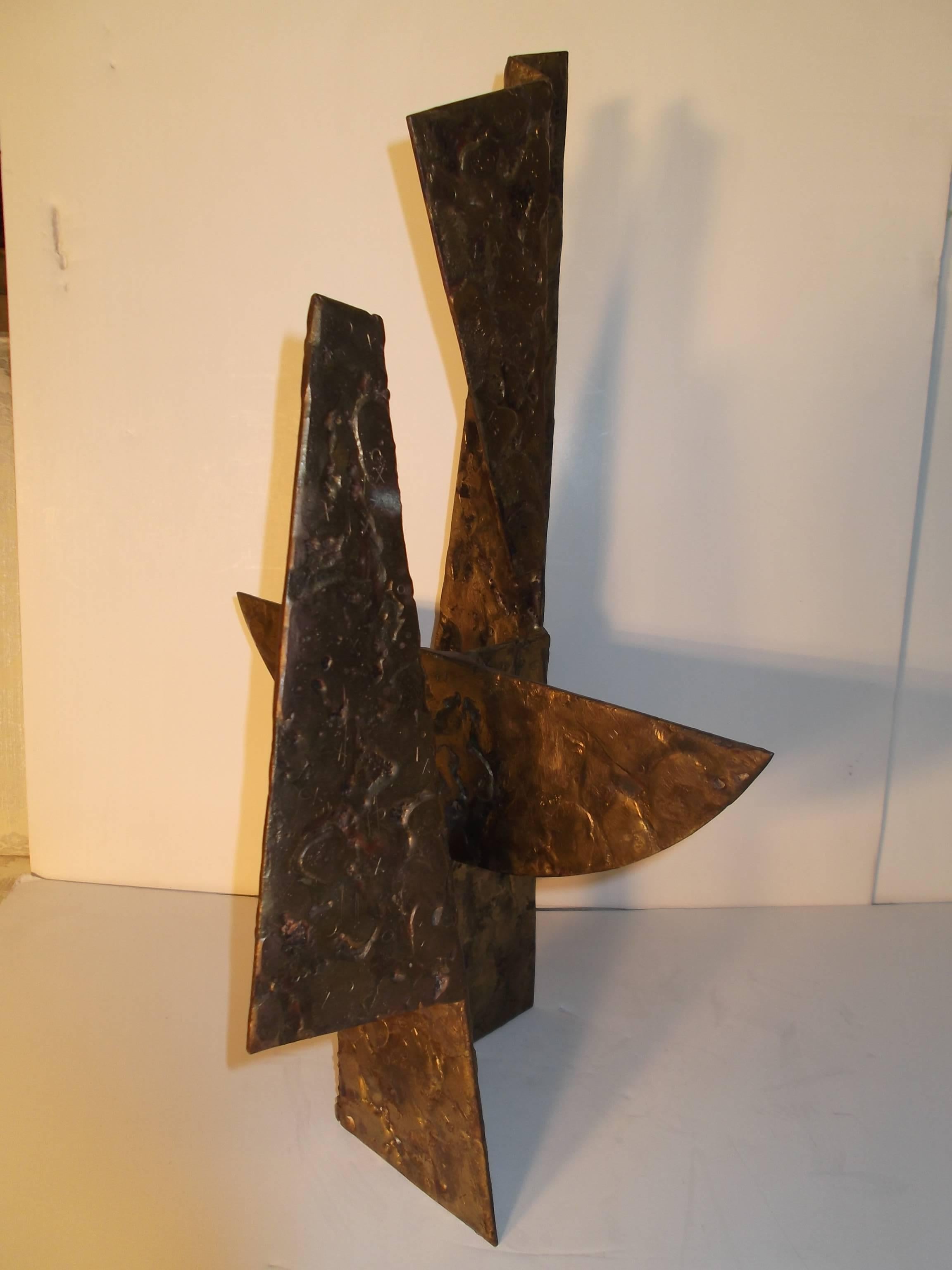 Signed to top side edge, This piece sort of resembles a Zuni Knifewing Warrior. It has a golded bronzed on steel, textured surface. Upon close inspection, the artist has hammered in X's and O's to the surface. This is a late in life sculpture for